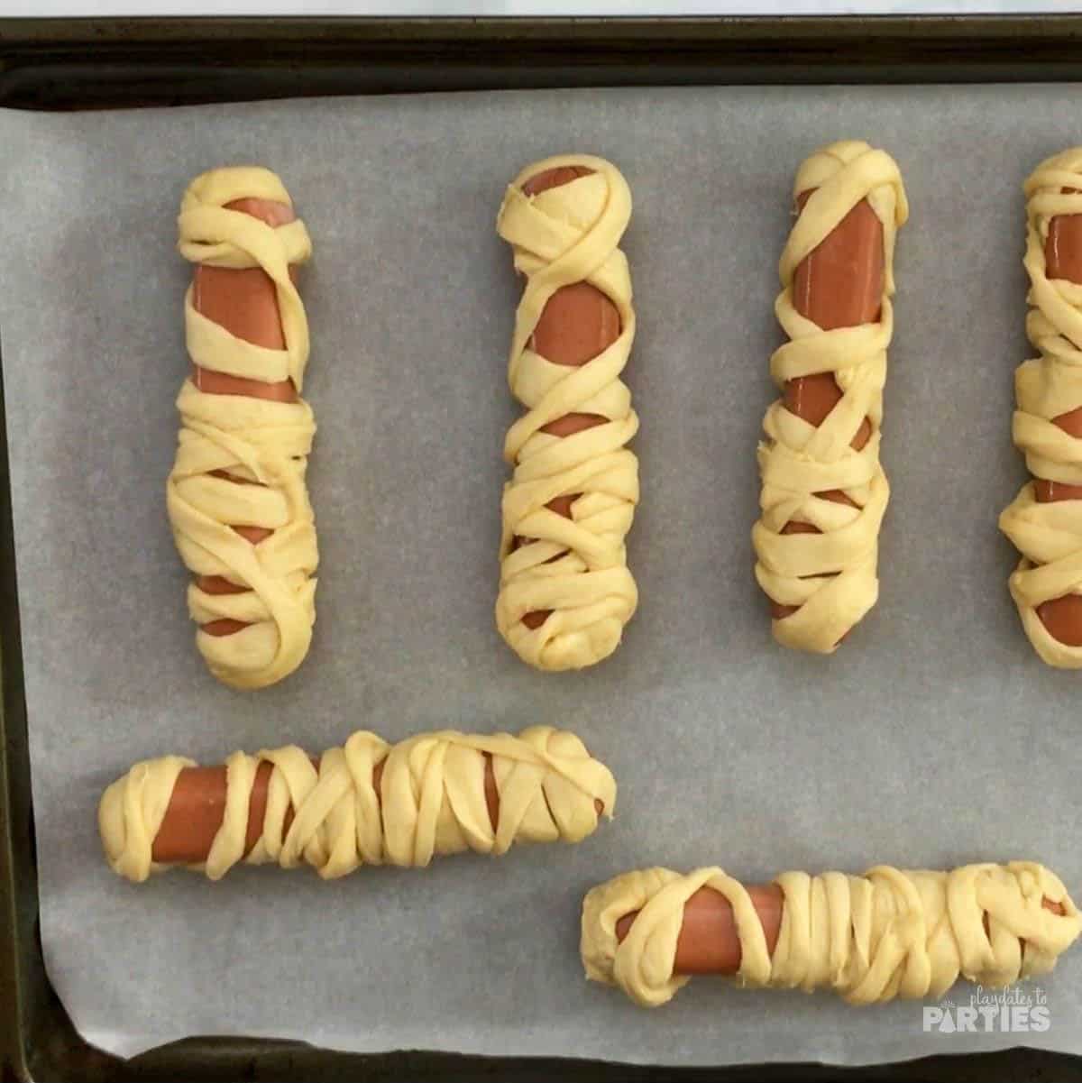 Uncooked mummy dogs on parchment paper.