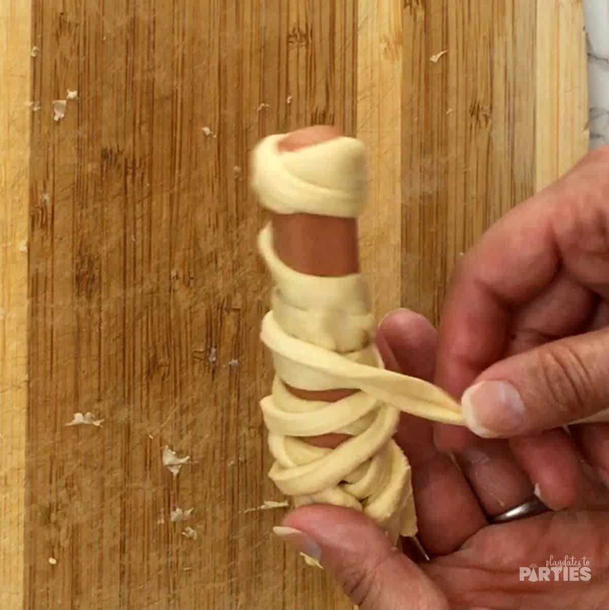 Wrapping a hot dog in dough to create a mummy.