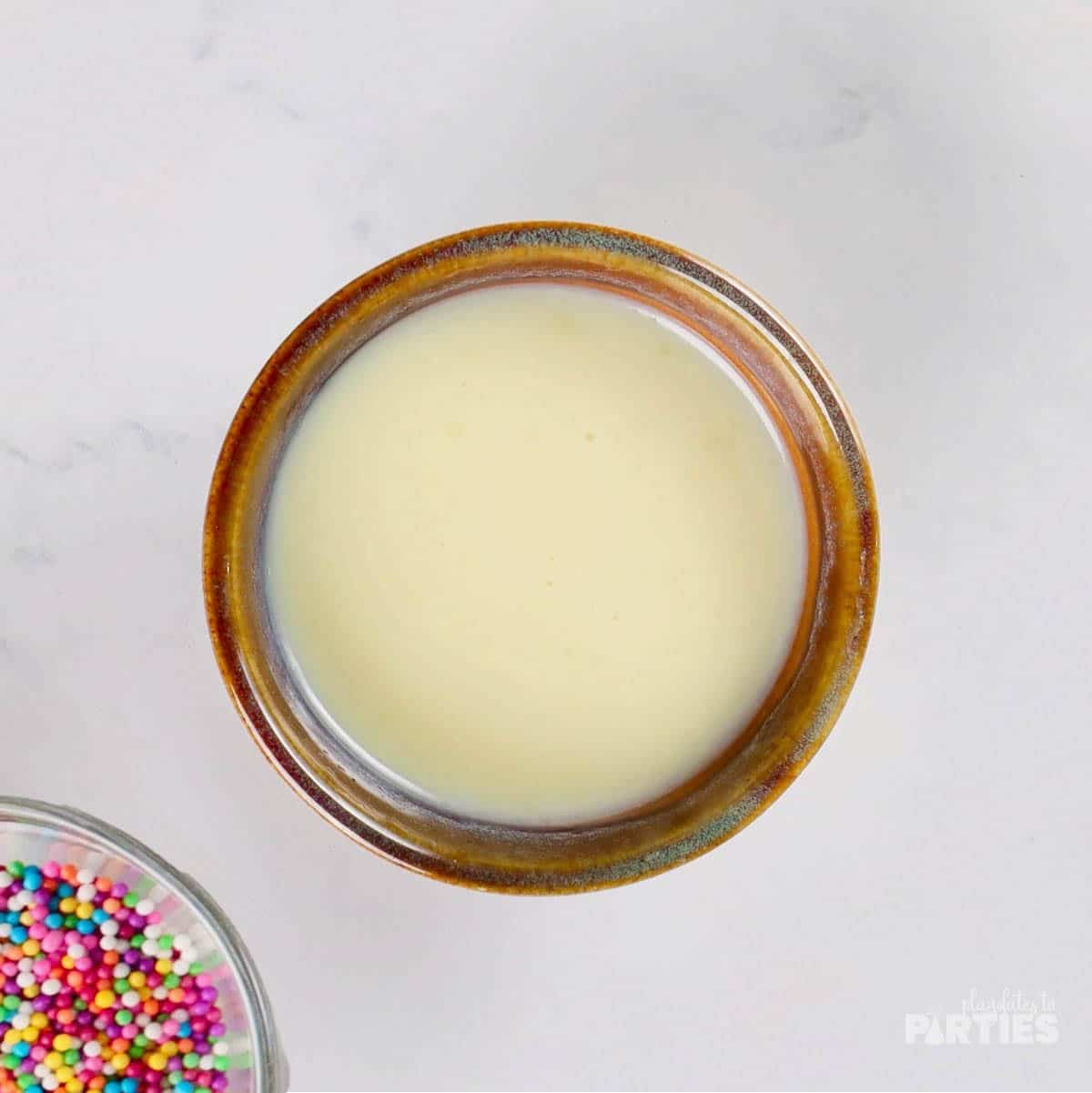 A small bowl of melted white chocolate with sprinkles nearby.