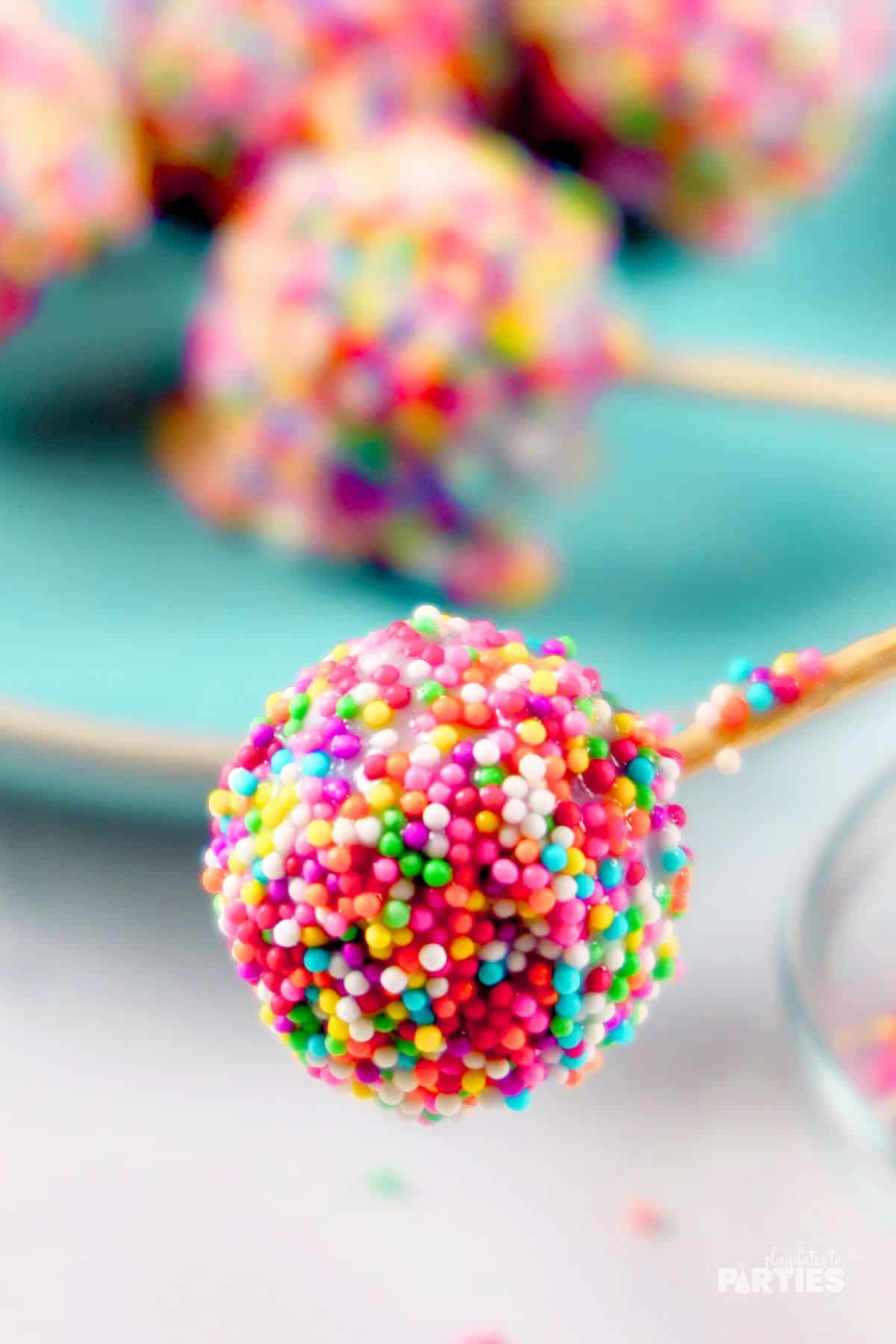 Close up view of a cake pop covered in rainbow sprinkles.