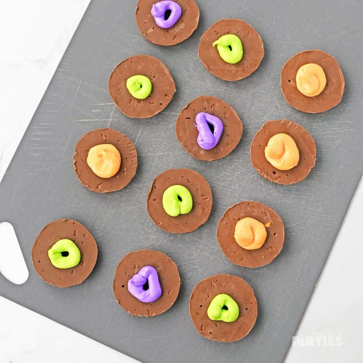 Colorful icing piped onto the bottom of chocolate covered cookies.