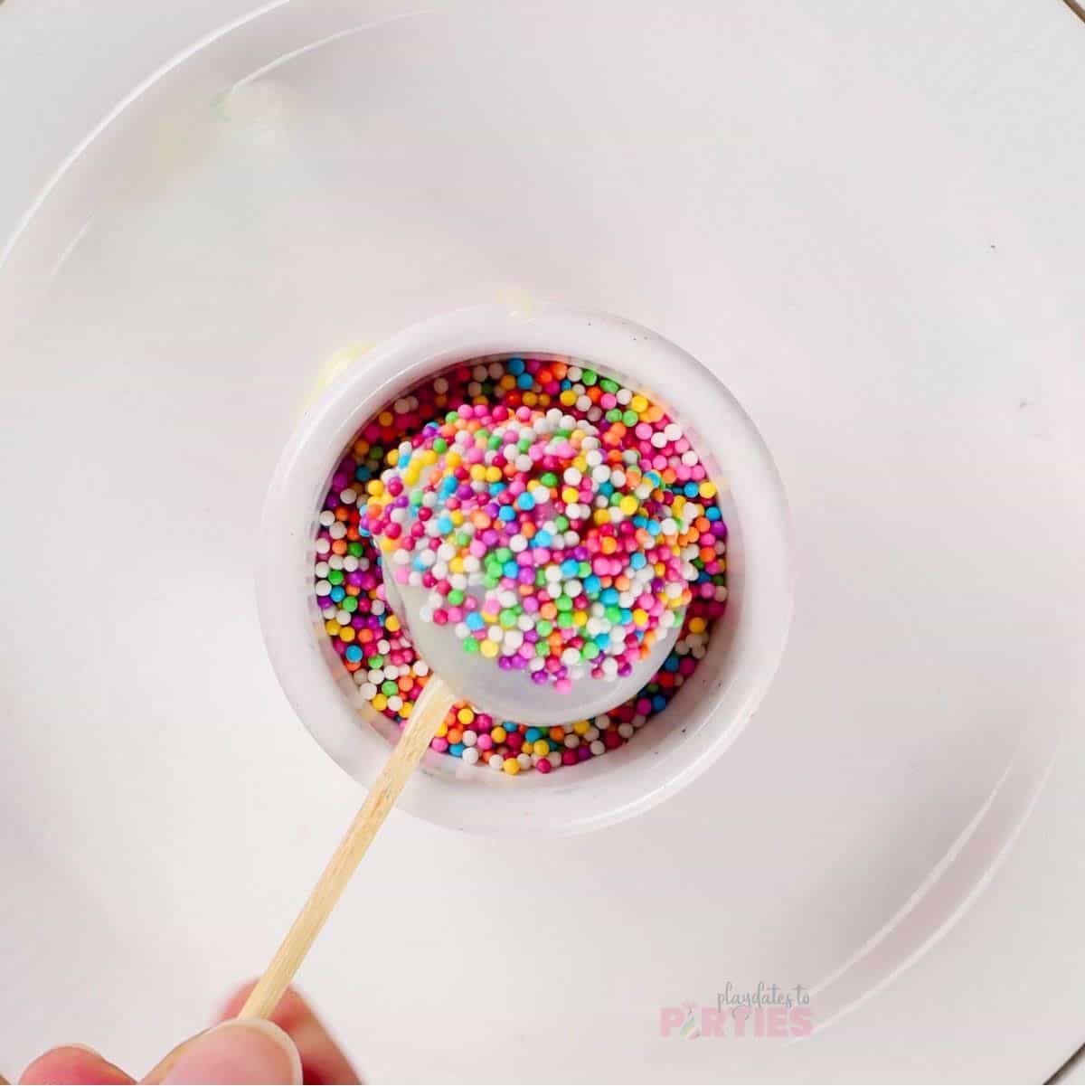 Dipping chocolate covered cake pops into sprinkles.