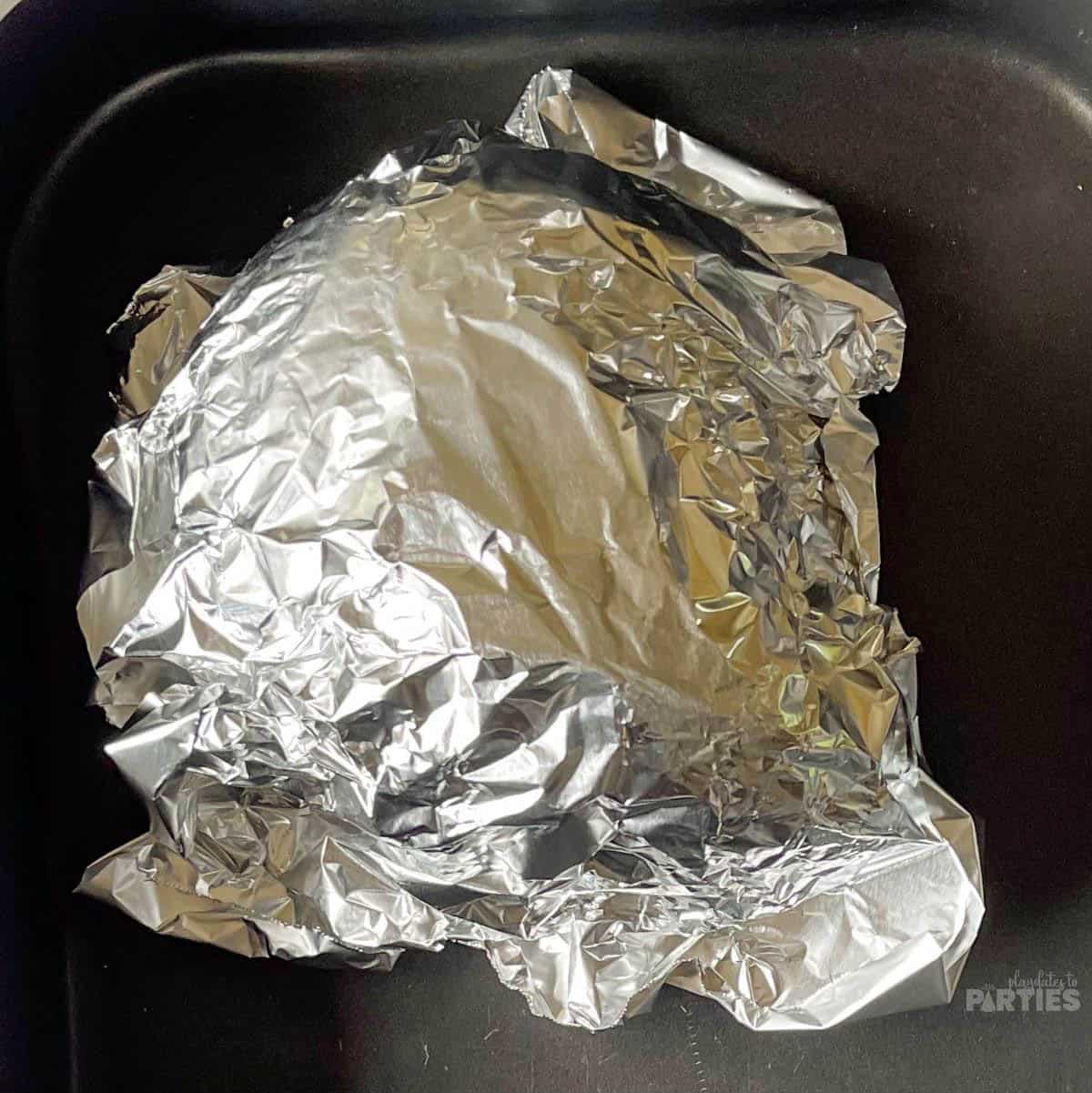 Ham wrapped in foil in a roasting pan.