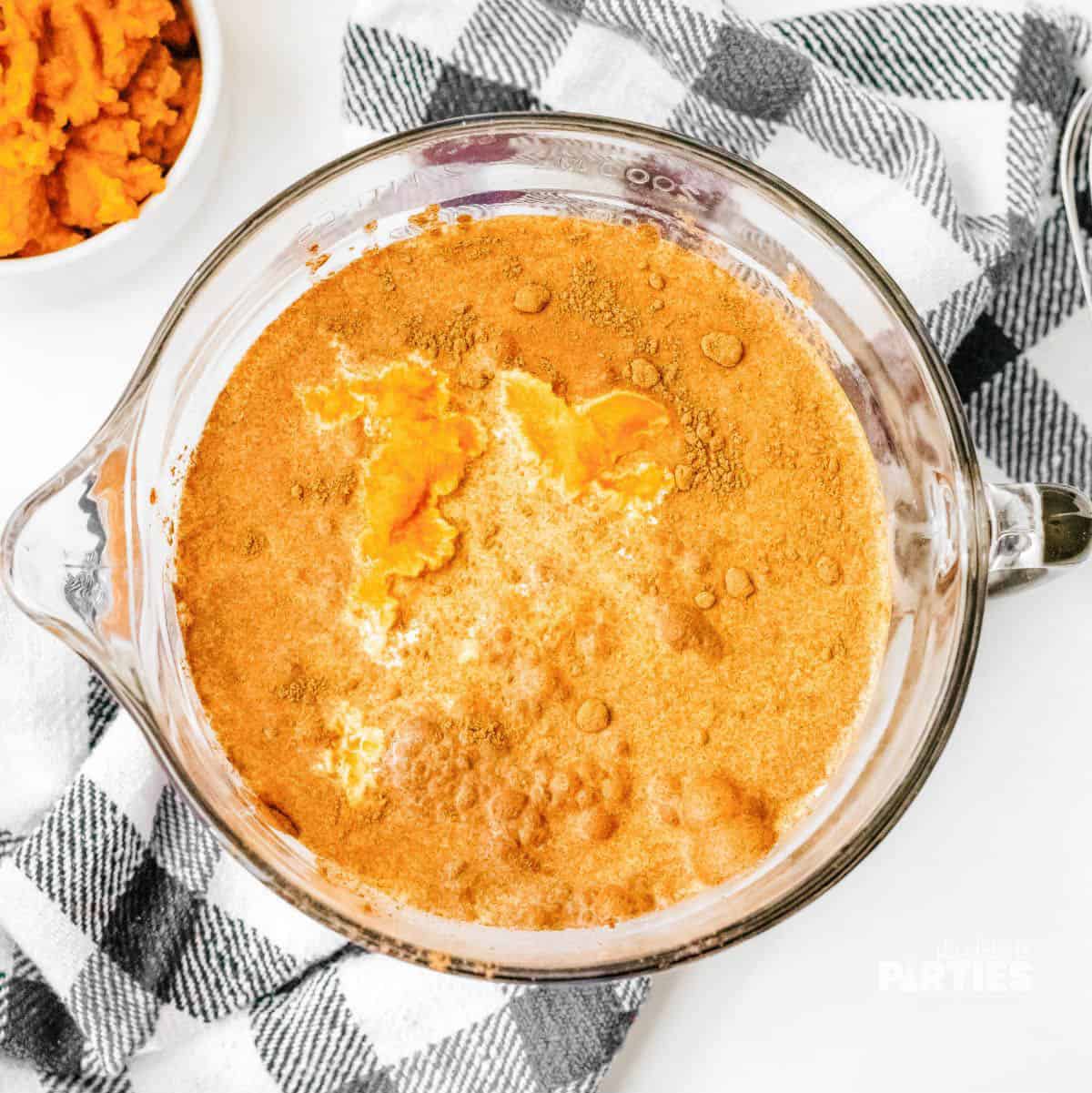 Pumpkin, spices, eggs, milk, and sugars in a bowl.
