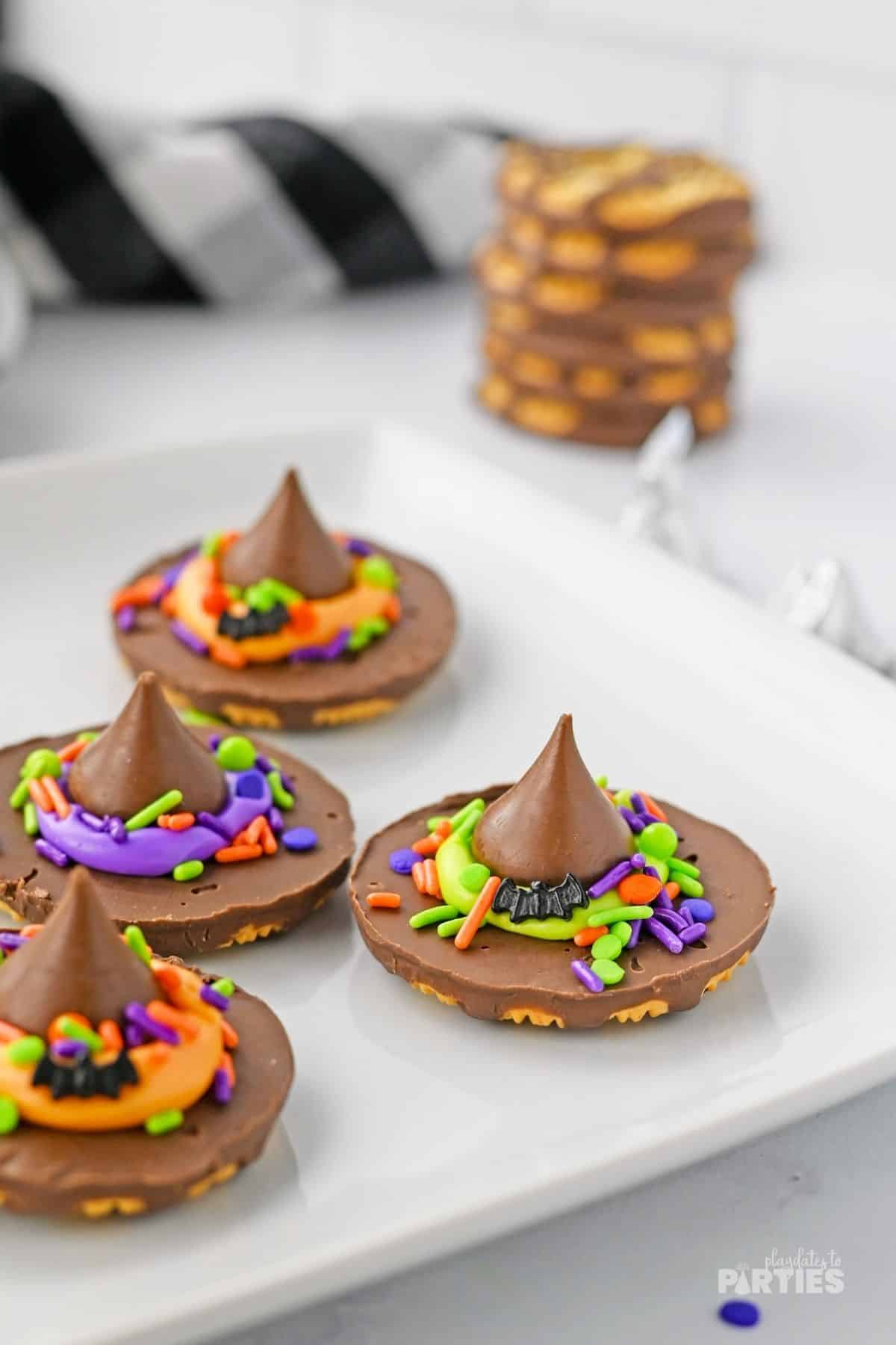 Witch hat cookies with orange, purple, and green sit on a white plate.