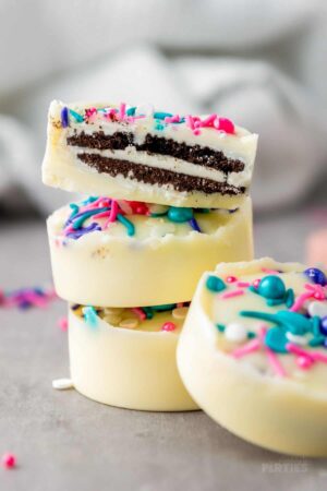 A stack of white chocolate covered Oreos with pink and blue sprinkles.