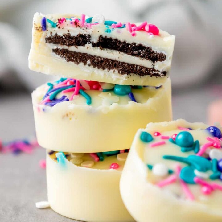 A stack of white chocolate covered Oreos with pink and blue sprinkles.