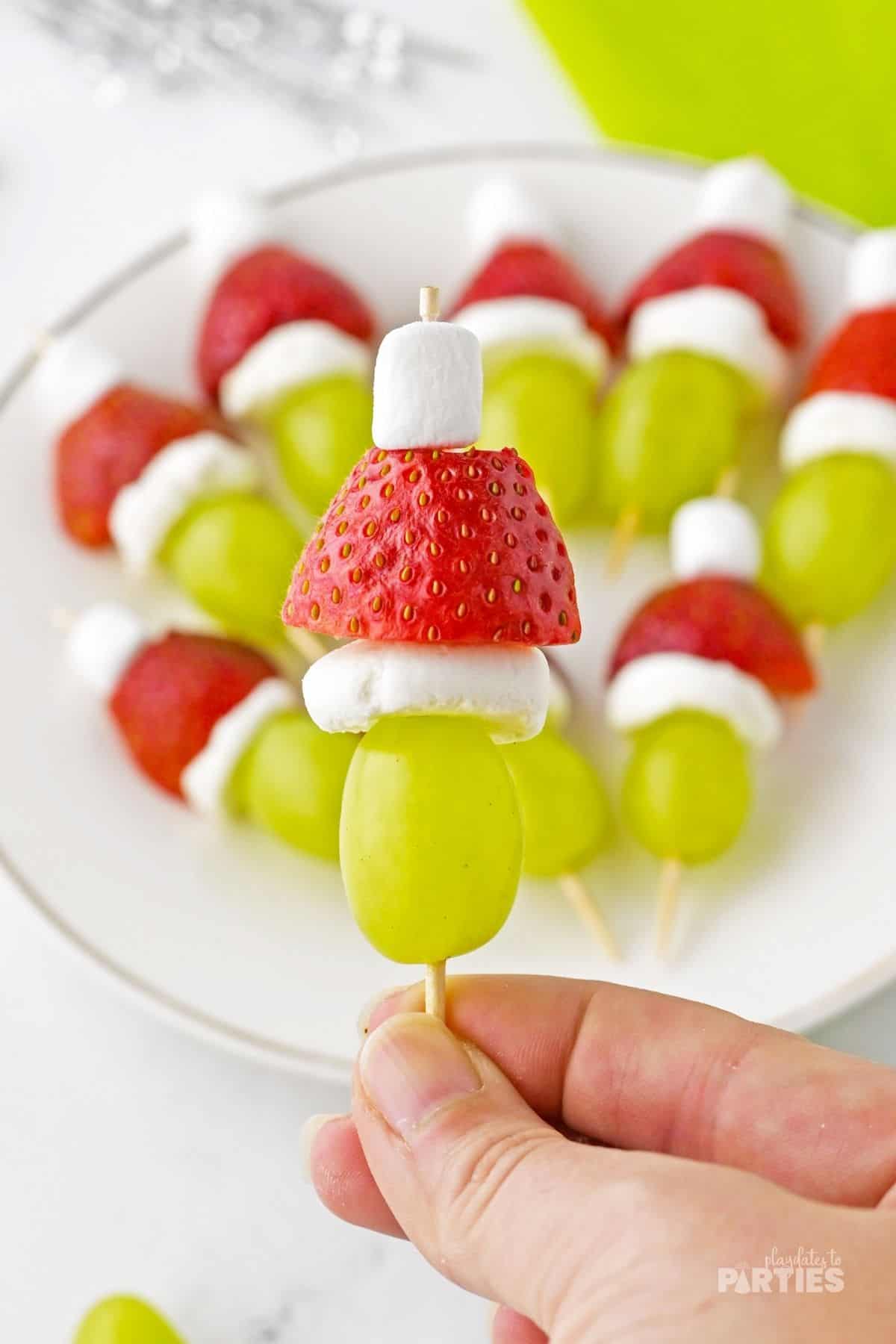 A woman's hand holding a Grinch themed fruit skewer.
