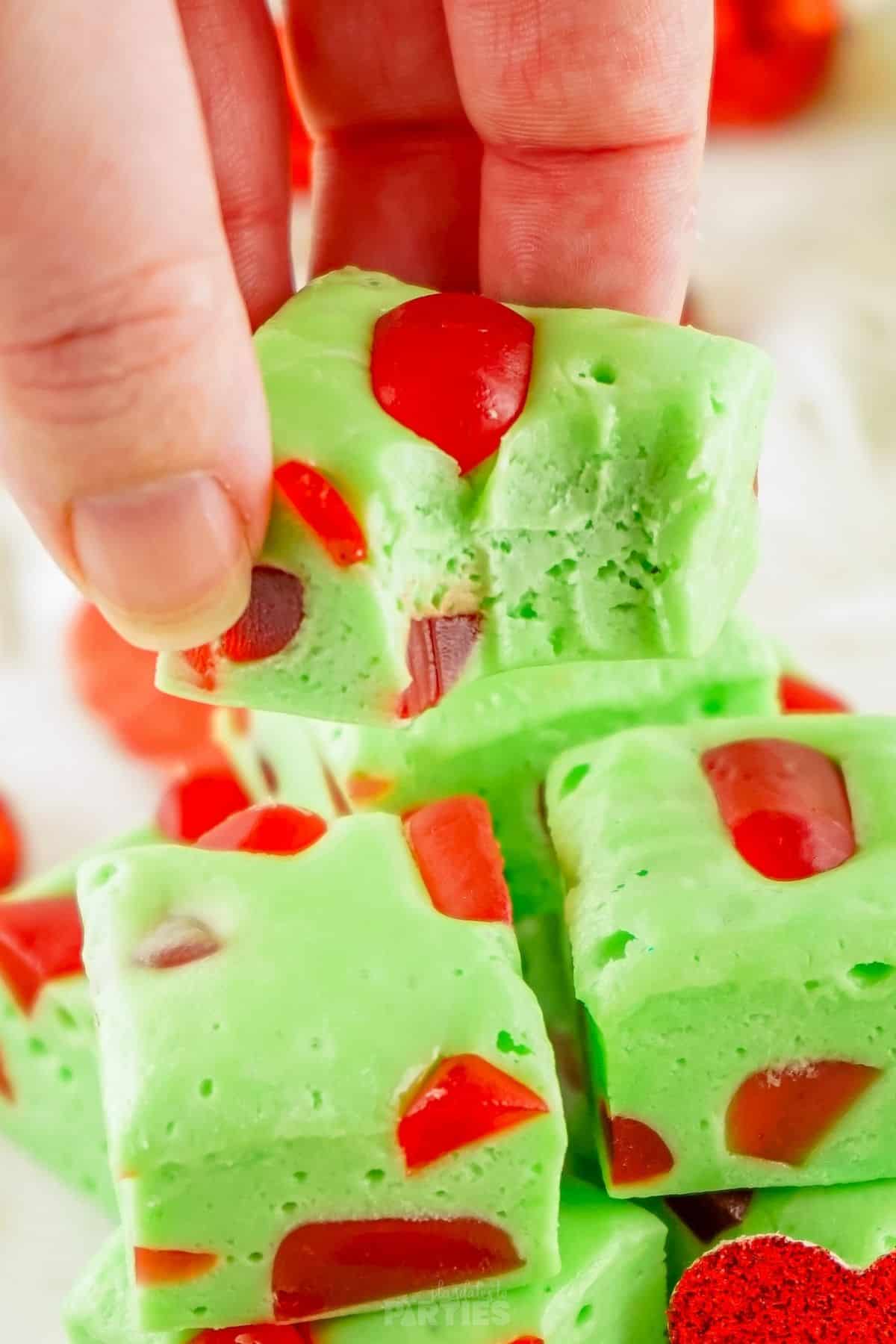 A woman's hand holds a piece of Grinch Christmas Nougat with a bite taken out.