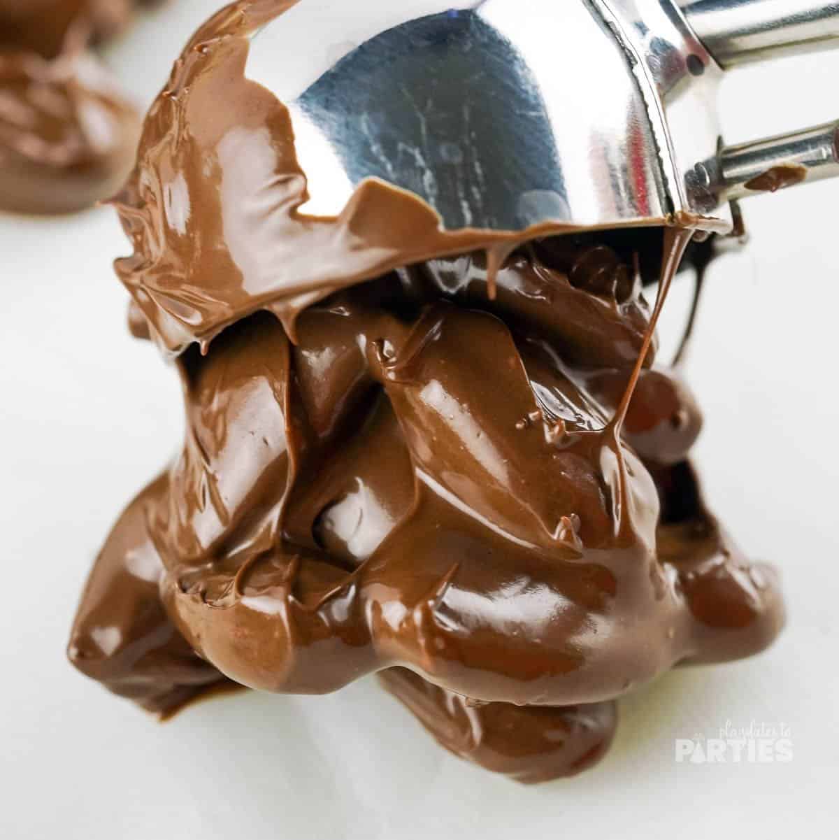 Scooping chocolate coated almonds onto parchment paper.
