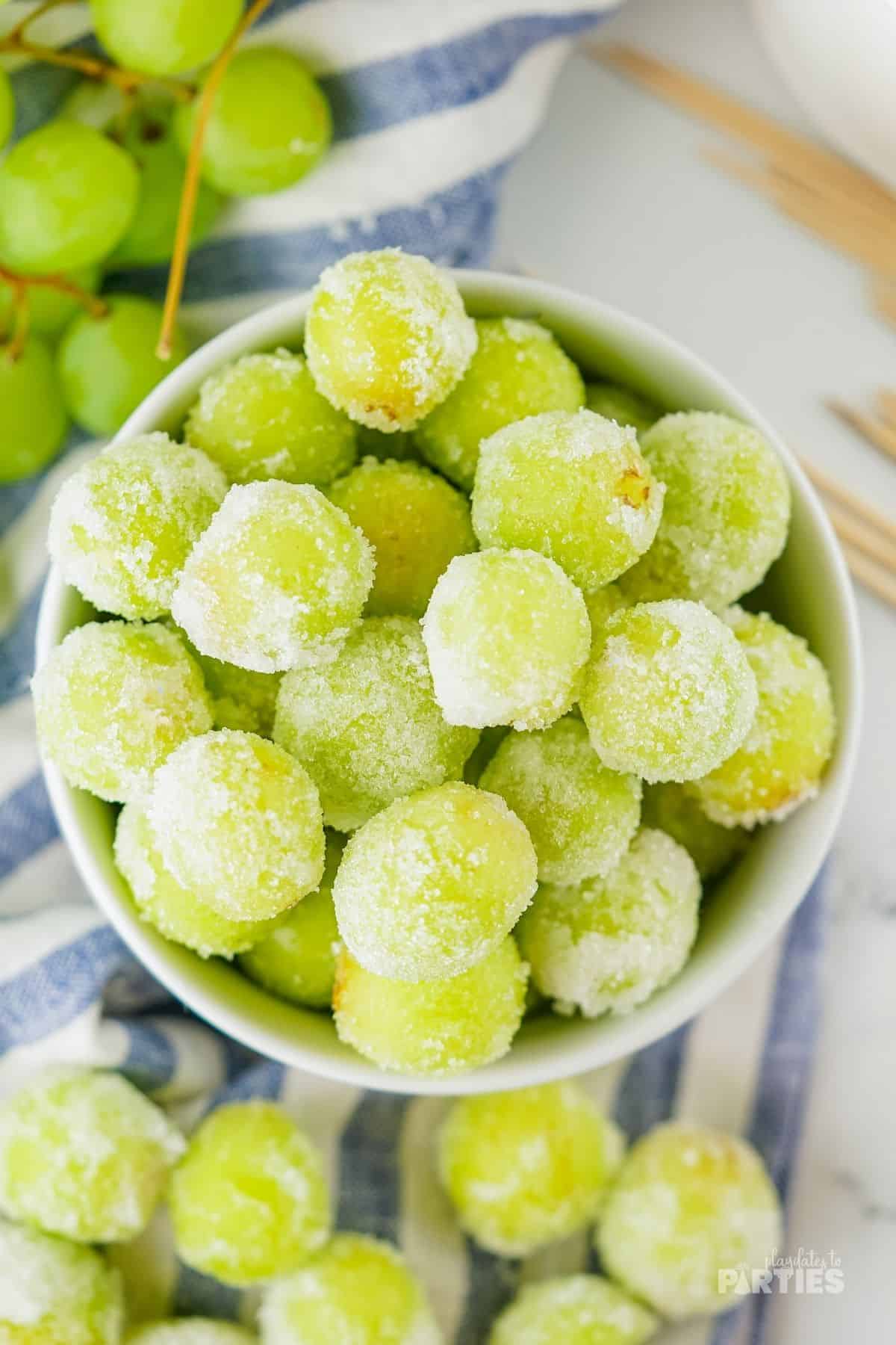A bowl of sugared champagne grapes with a blue striped tea towel underneath.