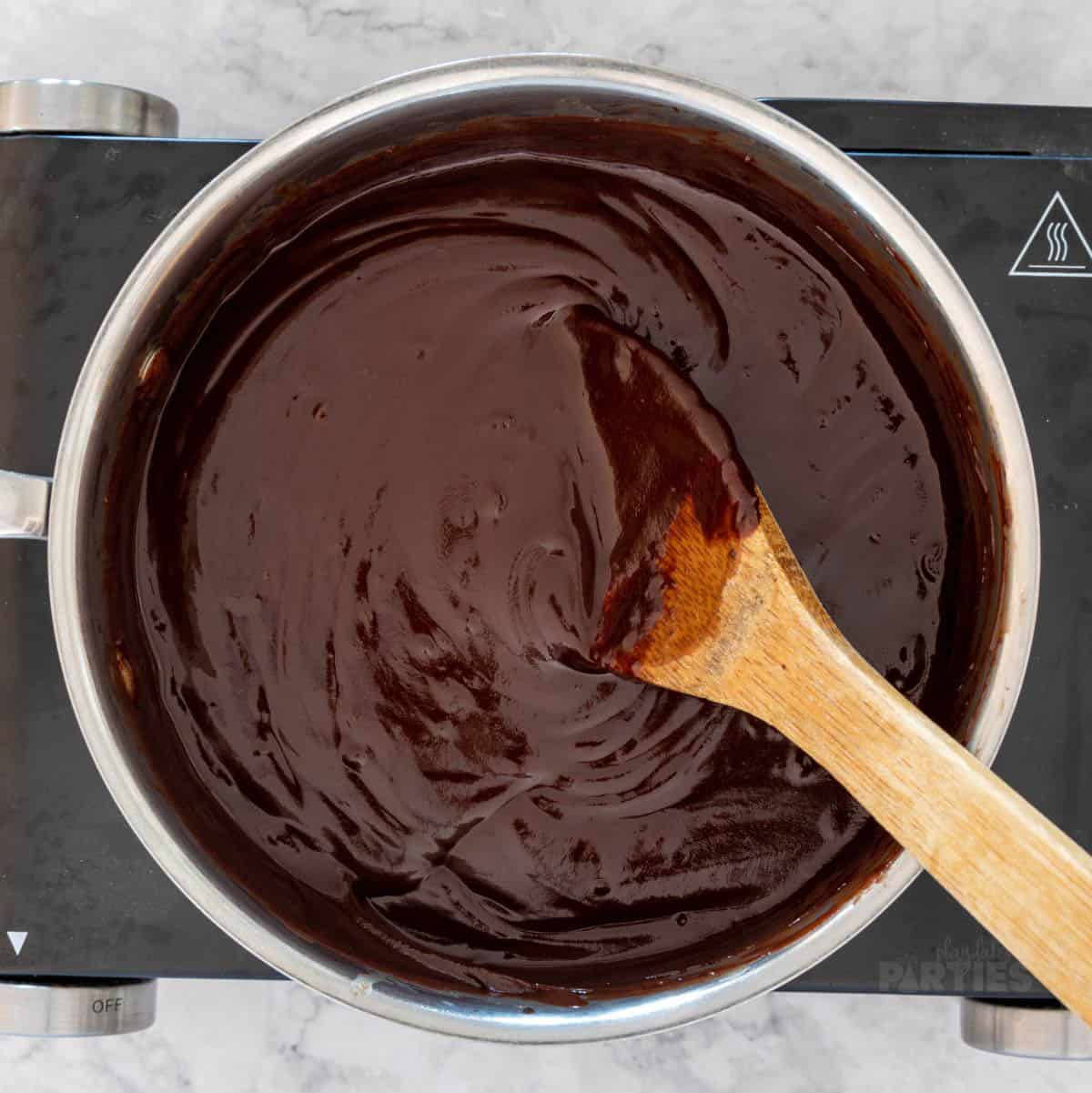 A pan of melted chocolate with a wooden spoon inserted in the middle.