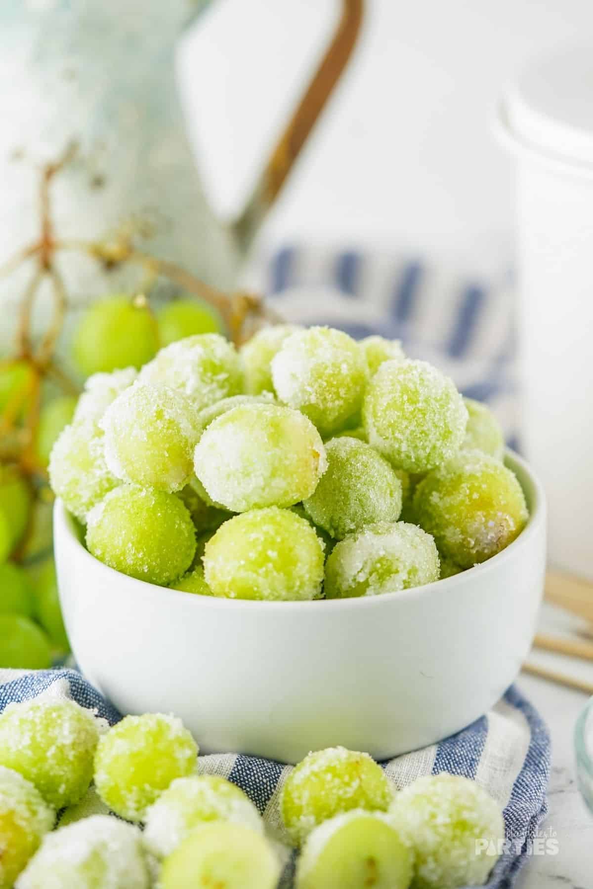 A white bowl is piled high with sugar coated champagne grapes.