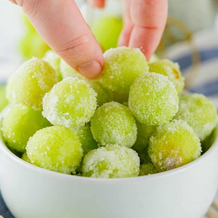 A woman's hand picking up a sugar coated green grape.