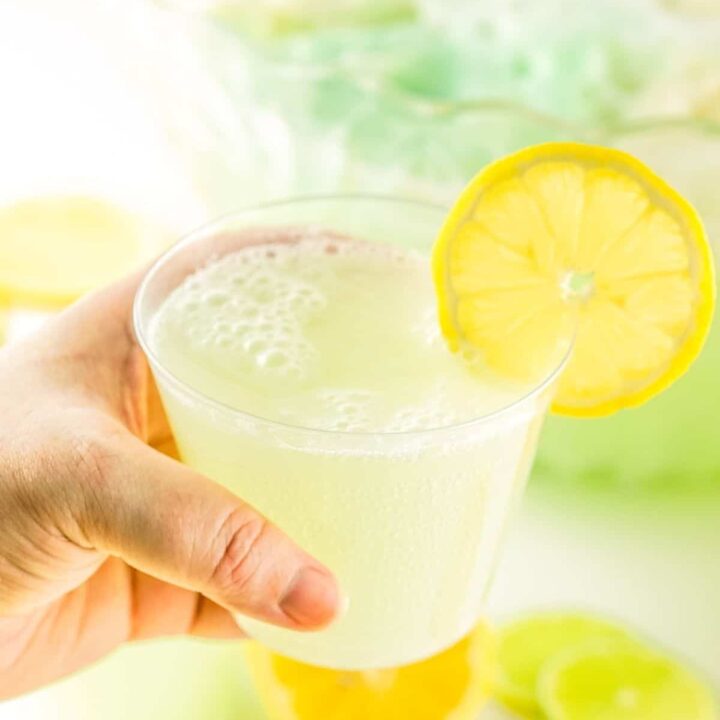 A woman's hand holding a cup of lemon lime party punch.