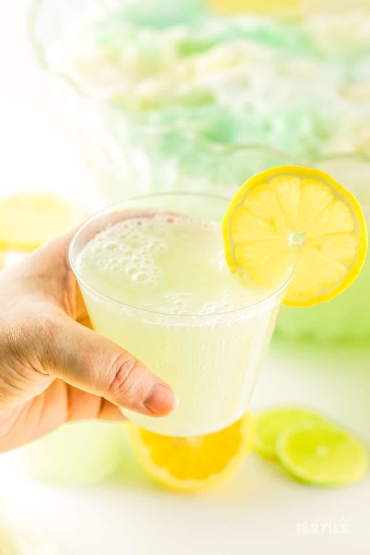 A woman's hand holding a cup of lemon lime party punch.