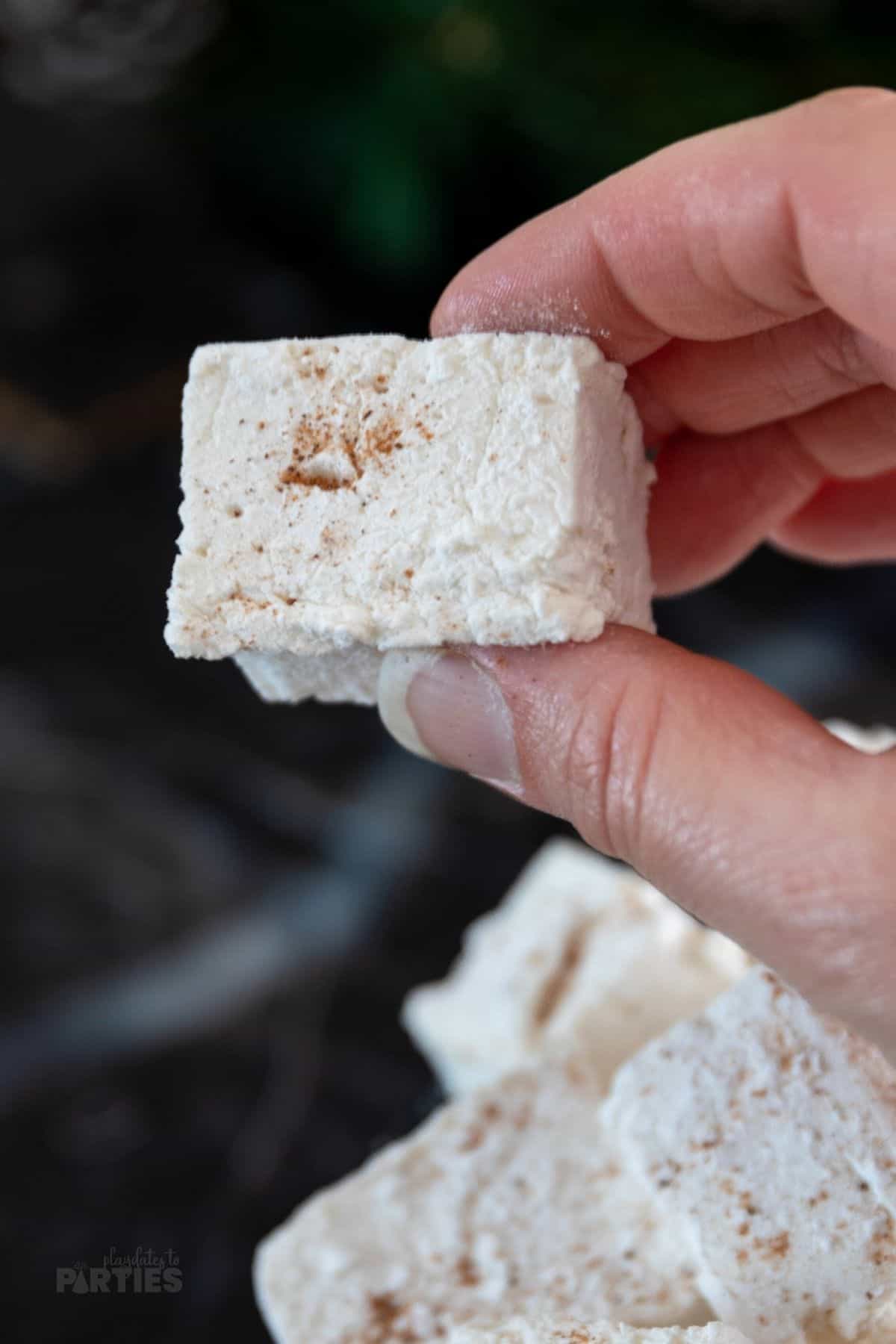 A woman's hand holding an eggnog marshmallow for Christmas.