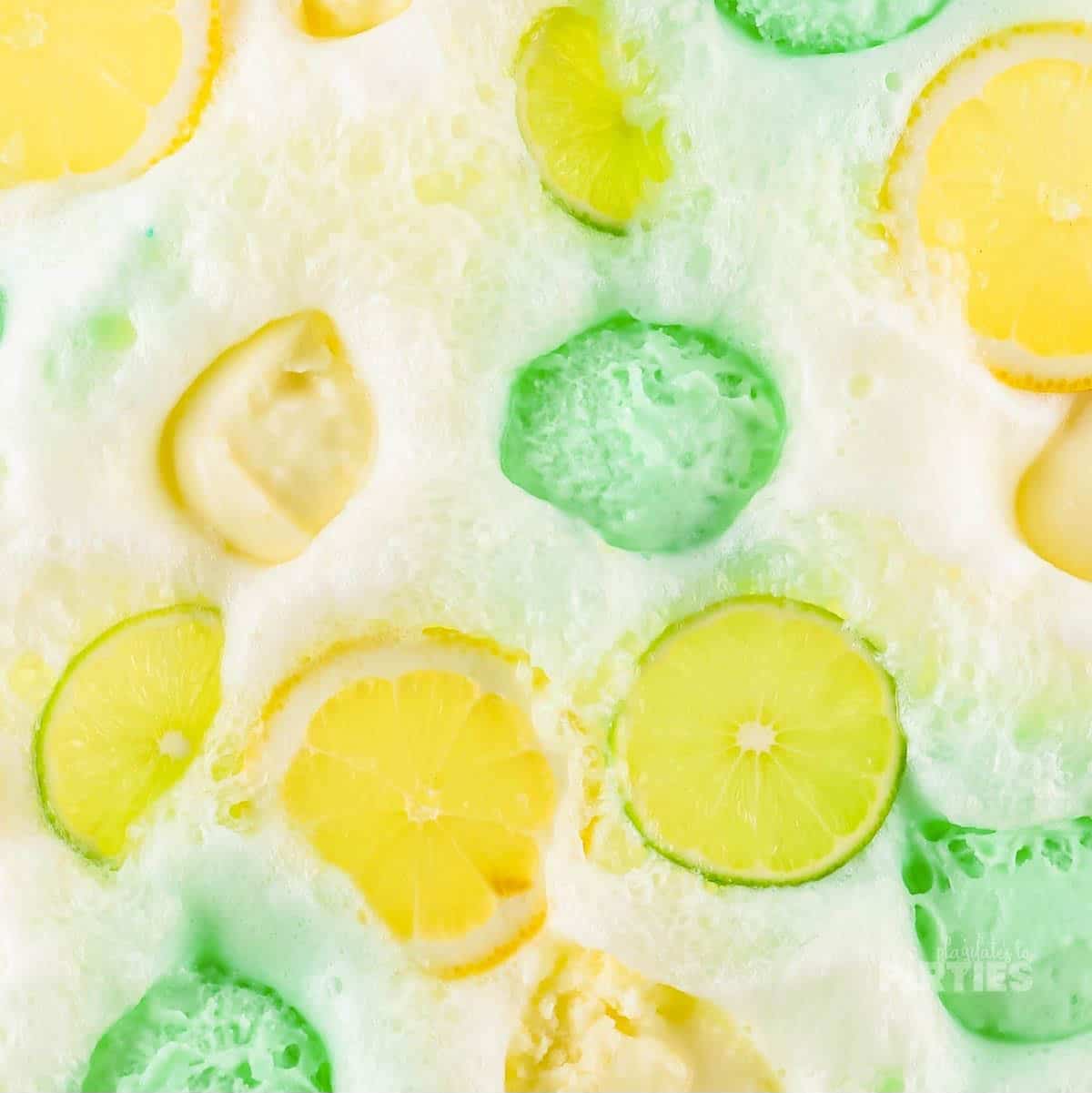 Scoops of yellow and green sherbet with lemon and lime slices floating in a punch bowl.