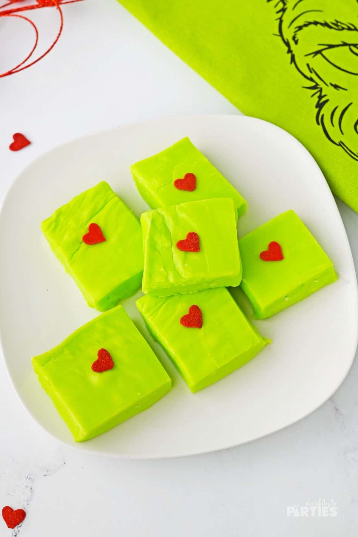 Six large squares of green Grinch Christmas fudge sit on a white plate.