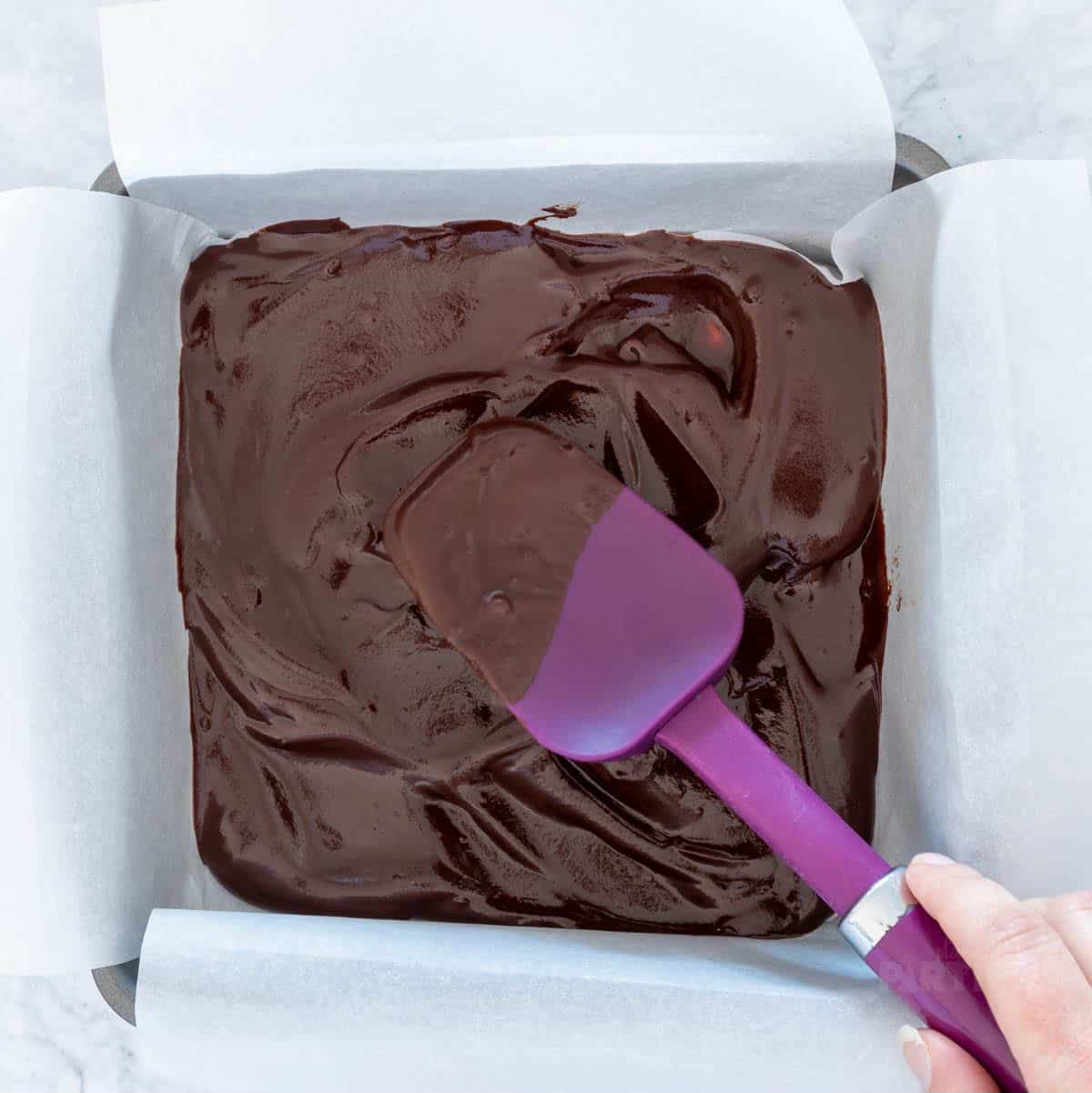 Spreading a thin layer of chocolate in a pan.