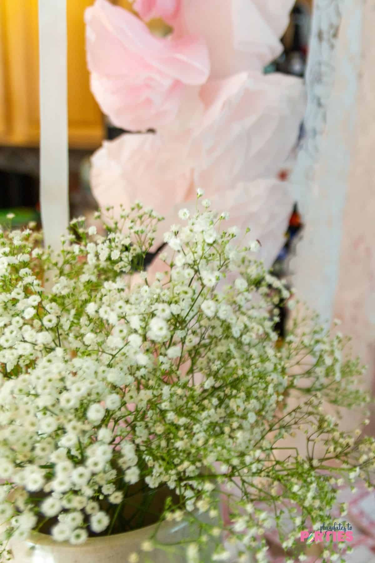 A vase of baby's breath sits in front of a fluffy coffee filter garland.