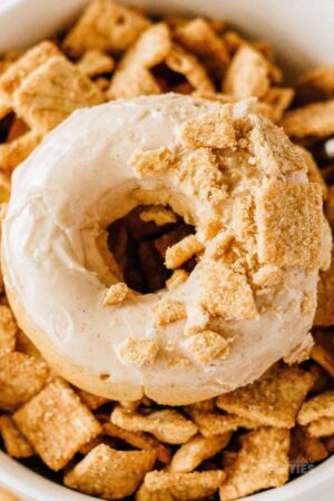 A baked glazed donut on top of a pile of Cinnamon Toast Crunch cereal.