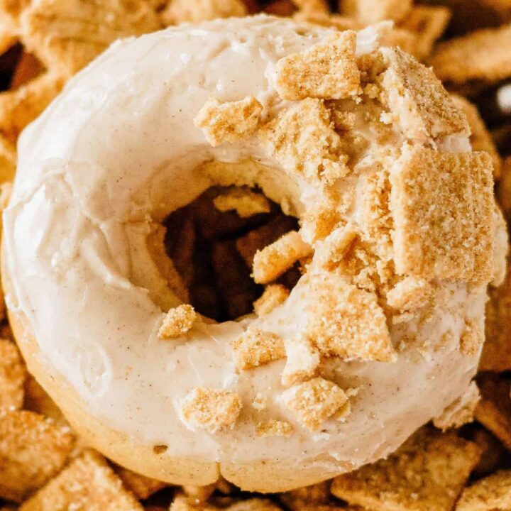 A baked glazed donut on top of a pile of Cinnamon Toast Crunch cereal.