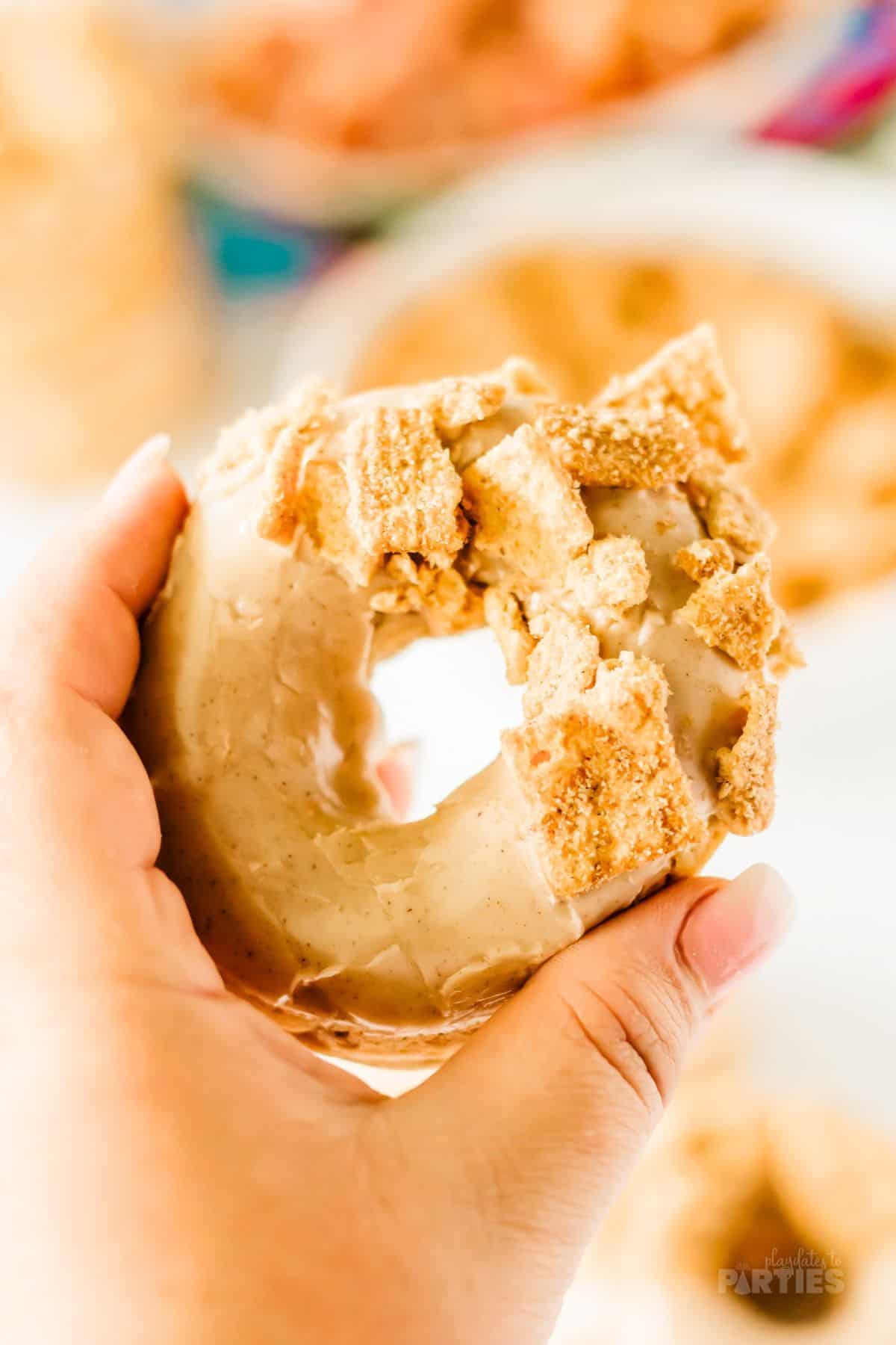 A woman's hand holding a Cinnamon Toast Crunch Cereal donut.