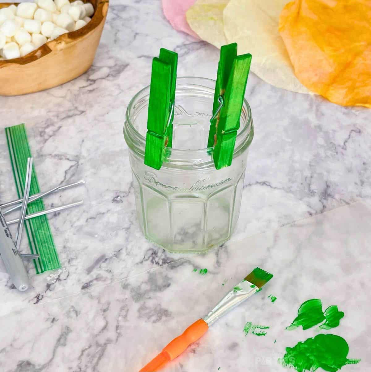 Green painted clothespins are clipped to a glass jar to dry.