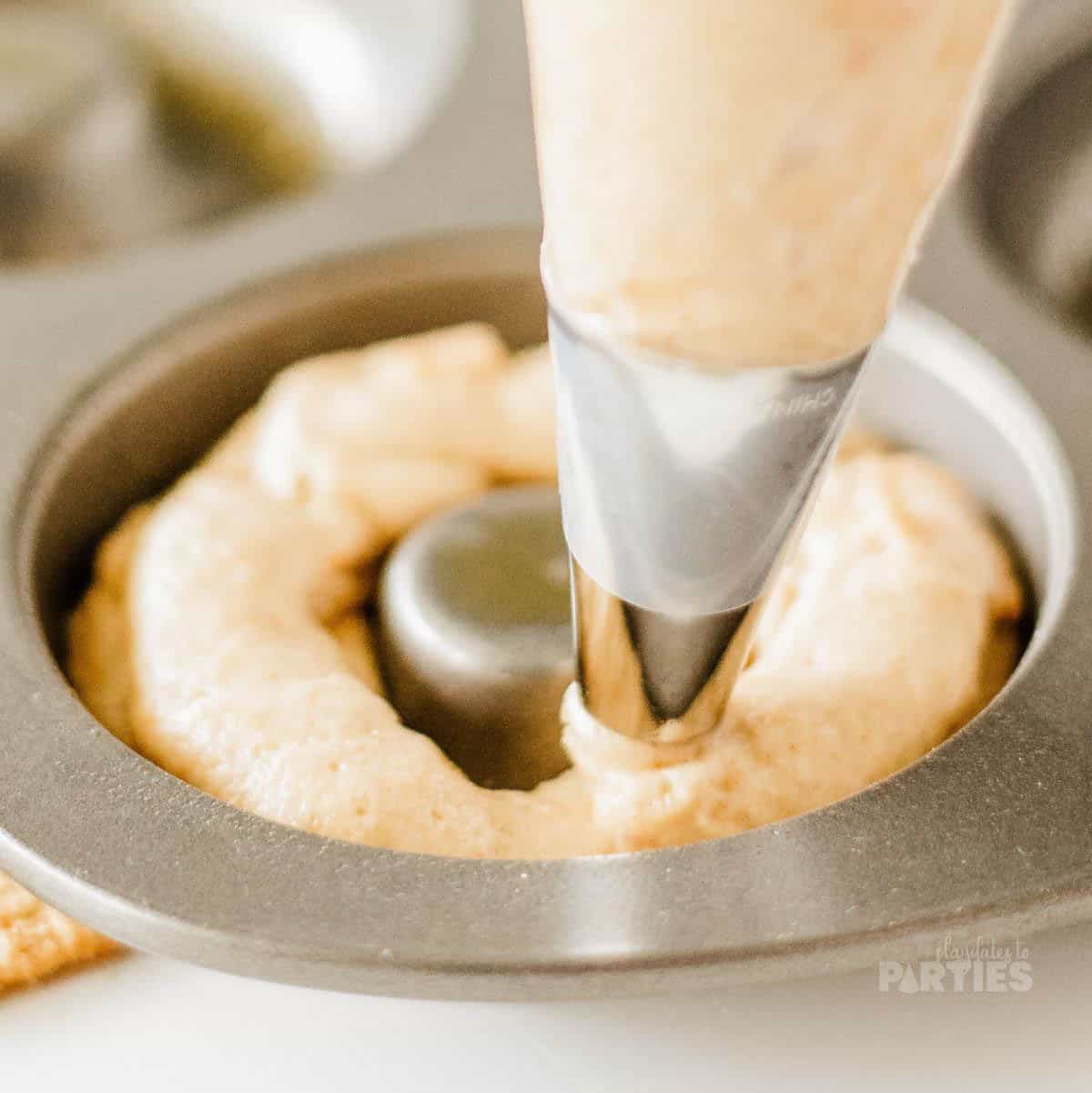 Using a piping bag to put donut batter into a pan.