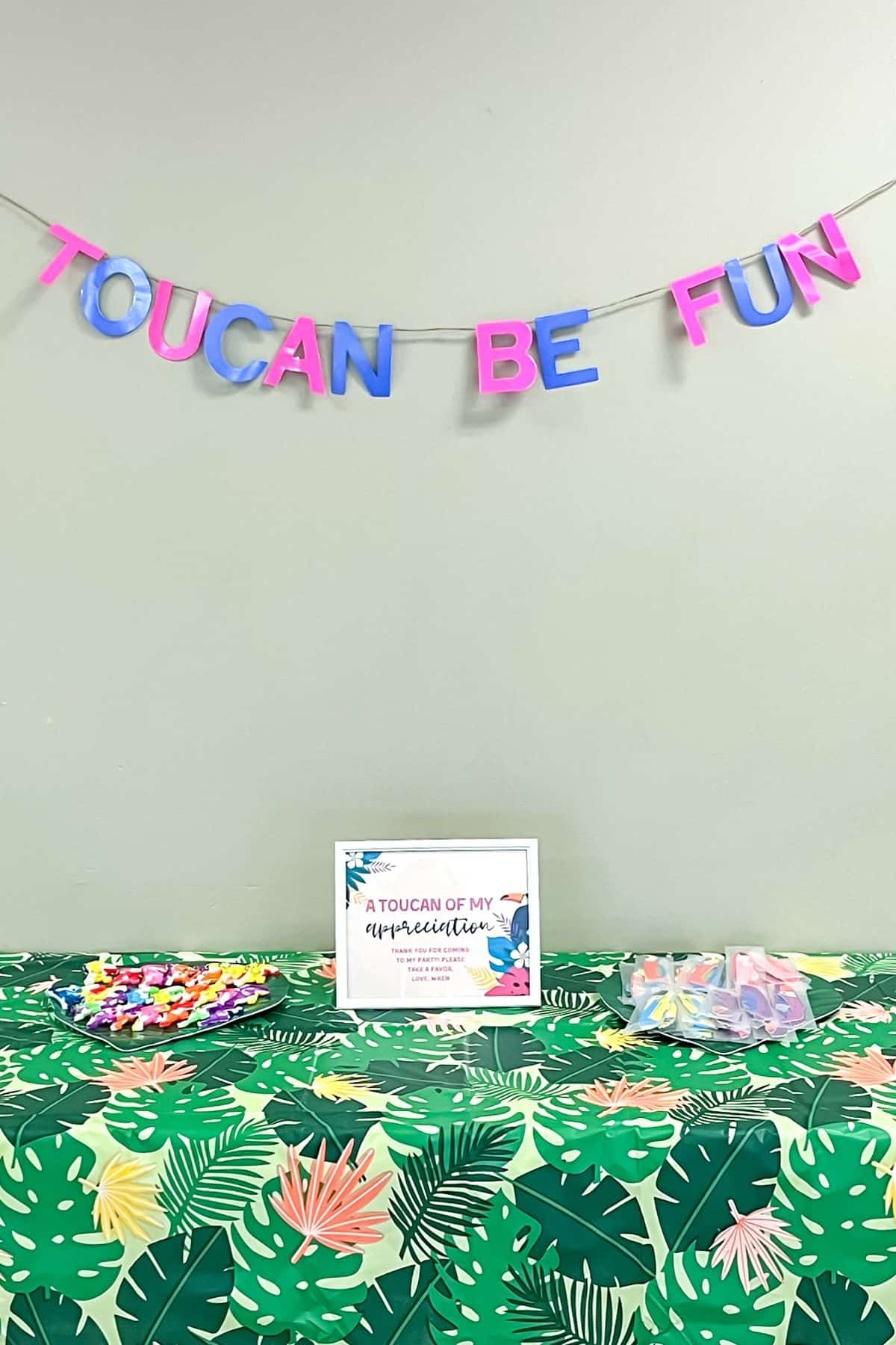 A party favor table with a banner that says toucan be fun.