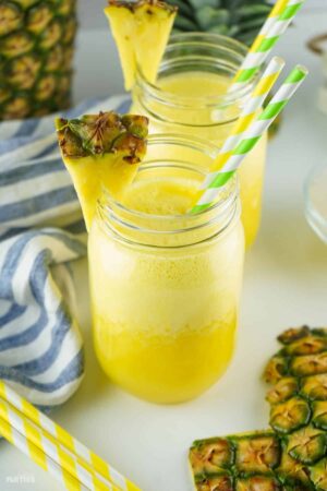 2 drinking glasses filled with pineapple agua fresca and garnished with fresh pineapple and paper straws.