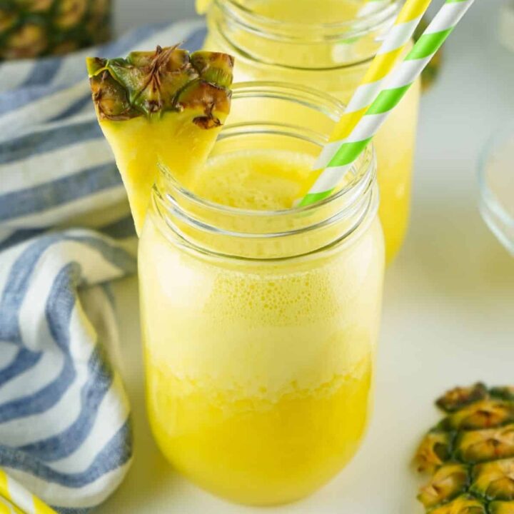 2 drinking glasses filled with pineapple agua fresca and garnished with fresh pineapple and paper straws.