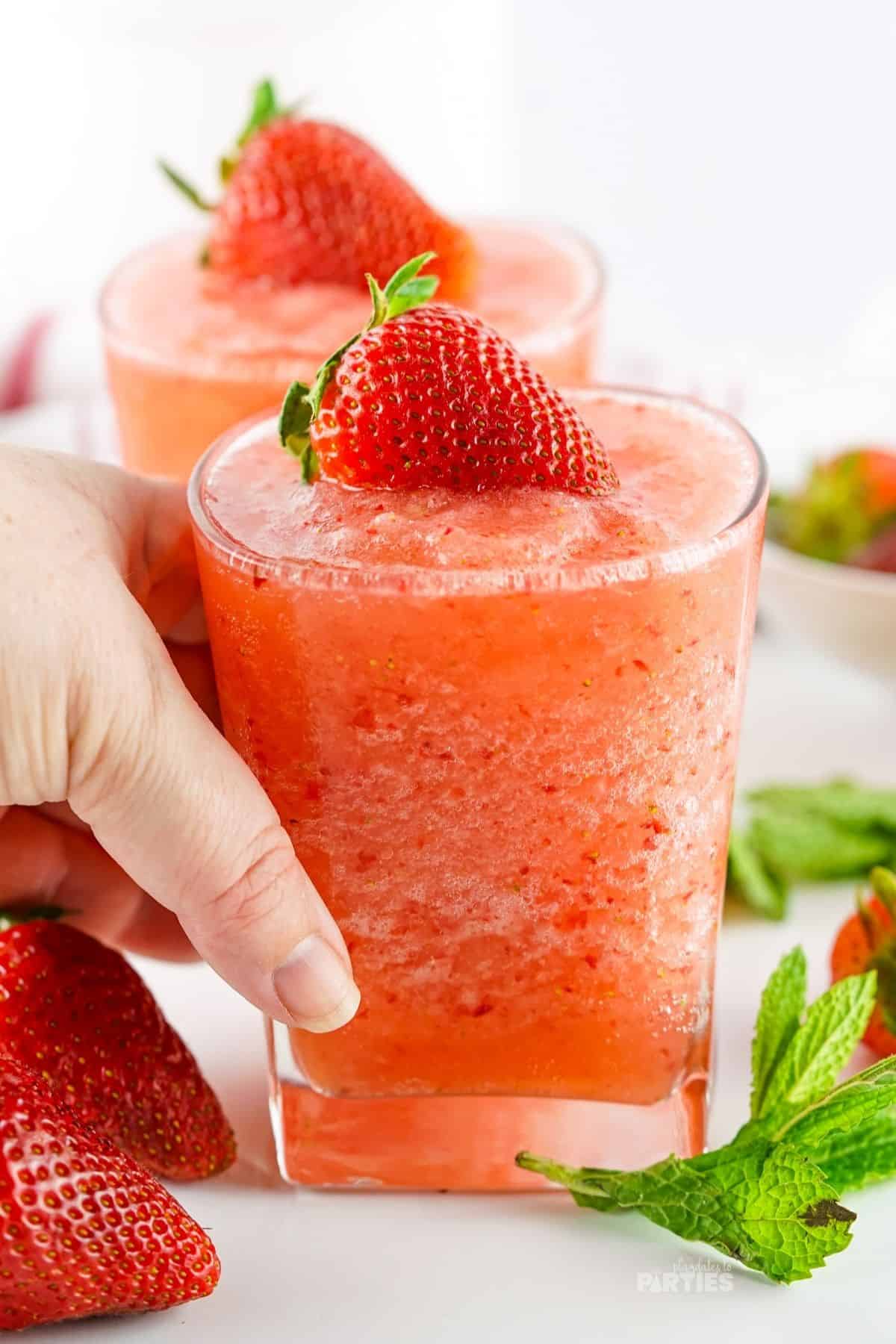A woman's hand holding a glass filled with a fruity frozen drink.