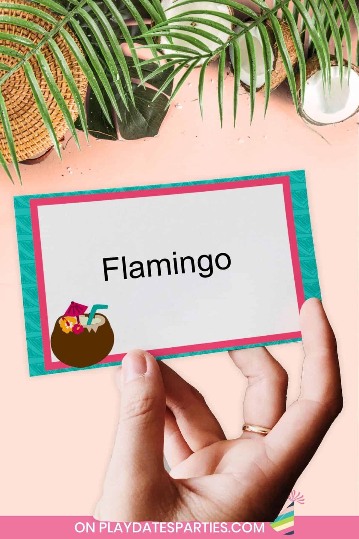 A woman's hand holding a luau themed charades card that says Flamingo.