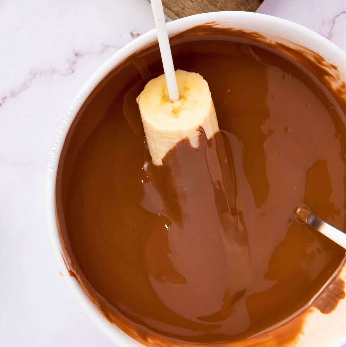 A banana half being dipped into melted chocolate.