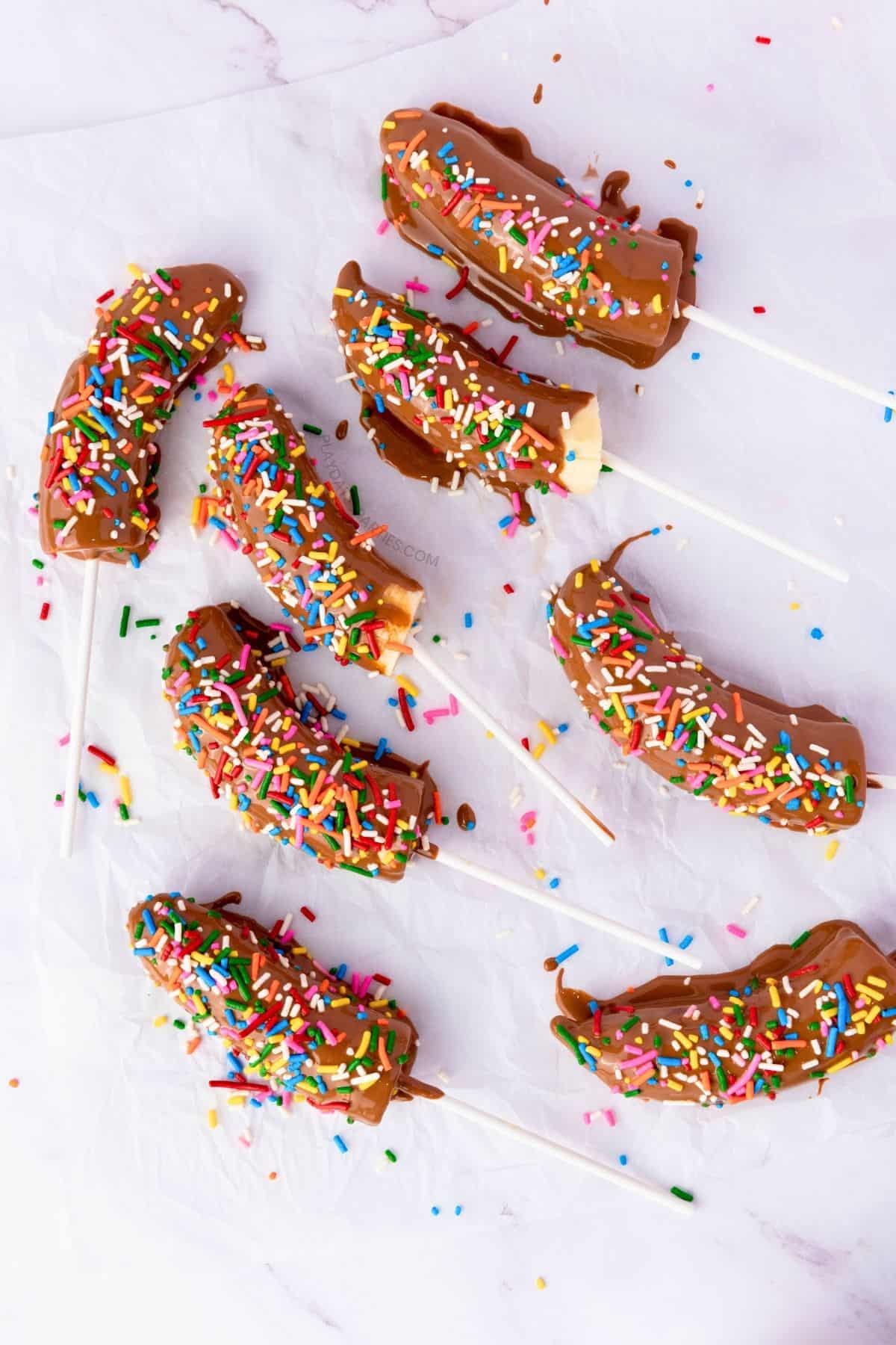 Several chocolate covered bananas on a marble surface.