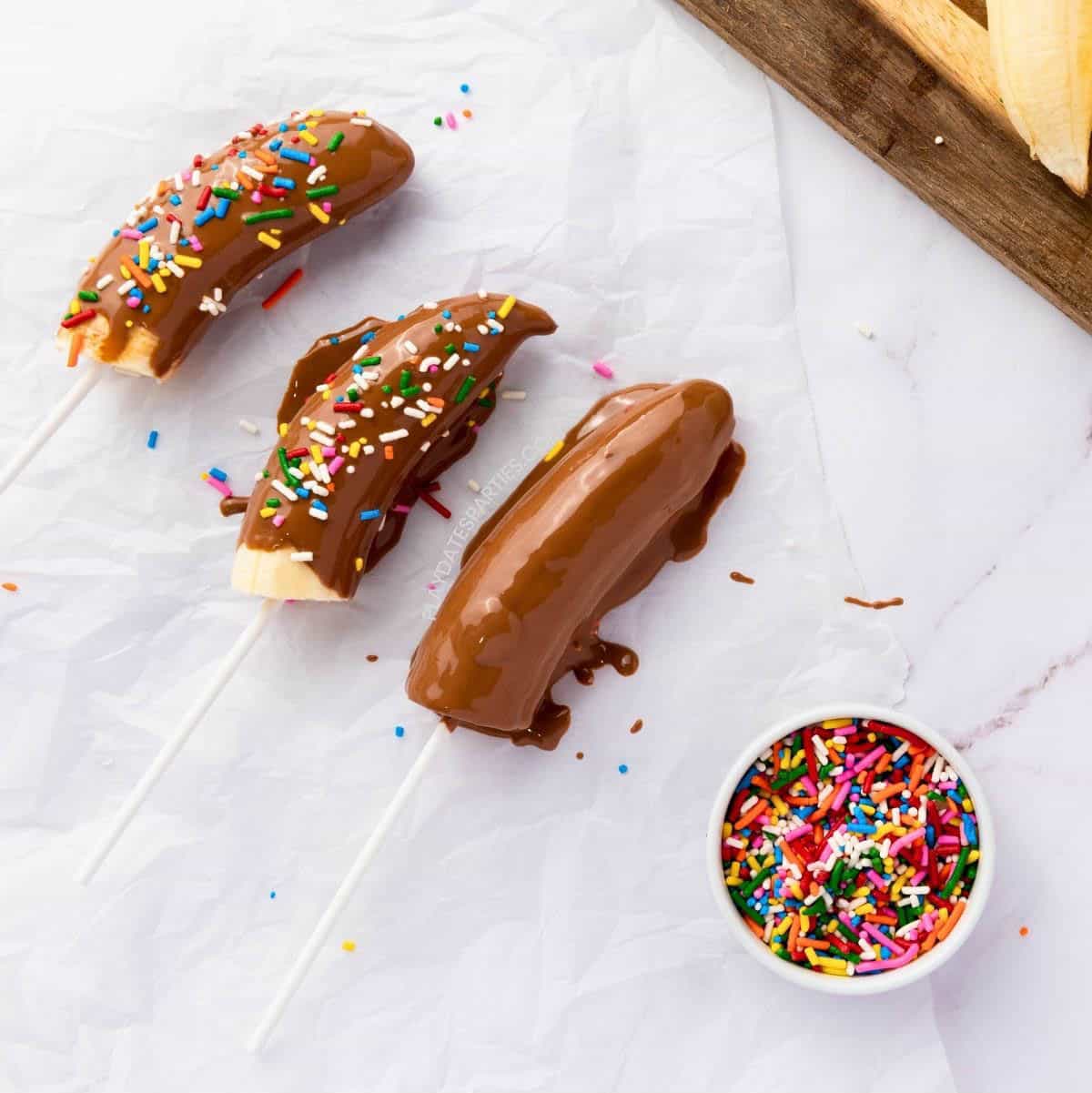 Three banana pops on parchment paper. Two have sprinkles on them.