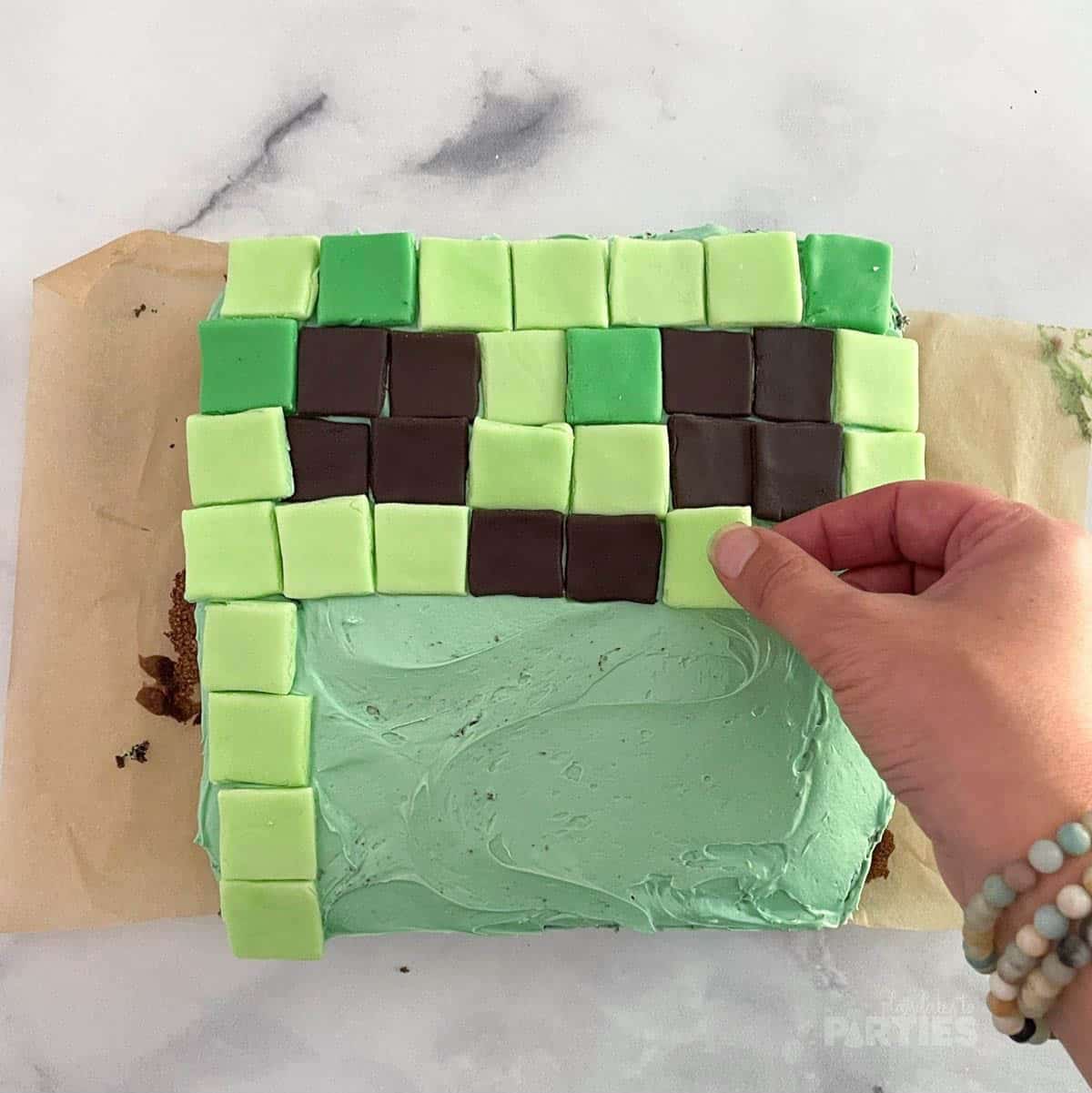 Placing fondant squares on a 9x9 cake to look like a Creeper face.