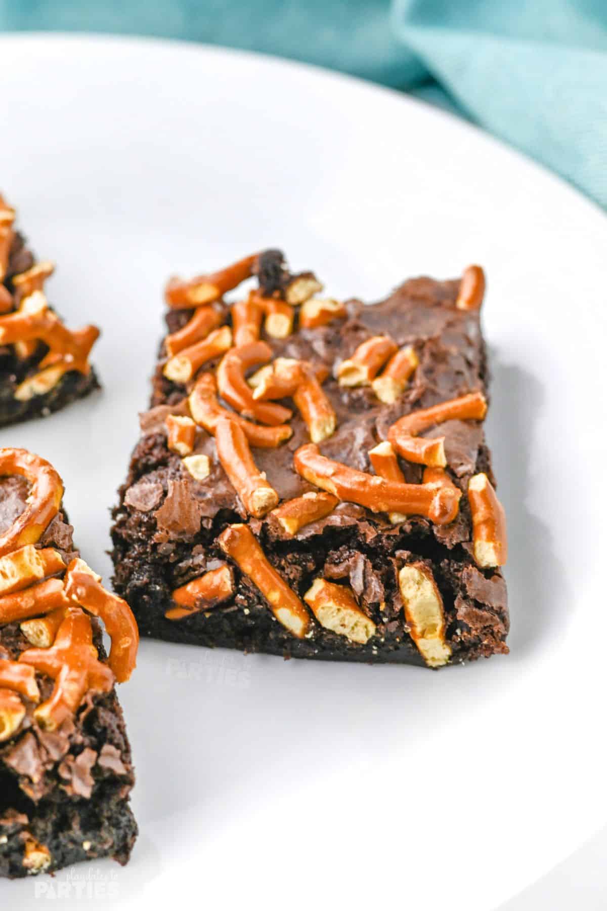 A brownie on a white plate with pretzels on top.