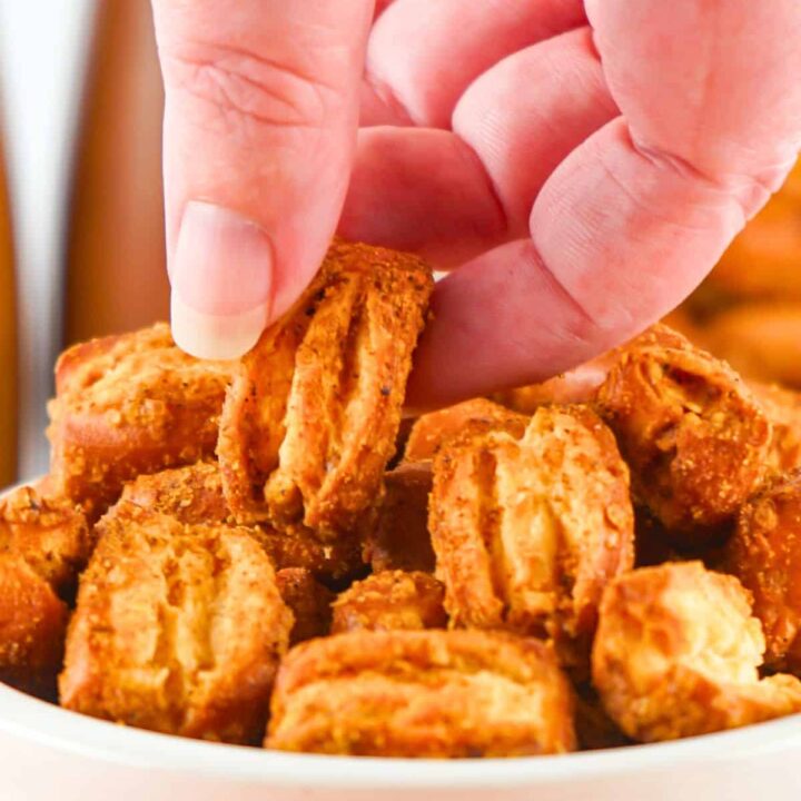 A womans hand grabbing pretzel bites from a bowl.