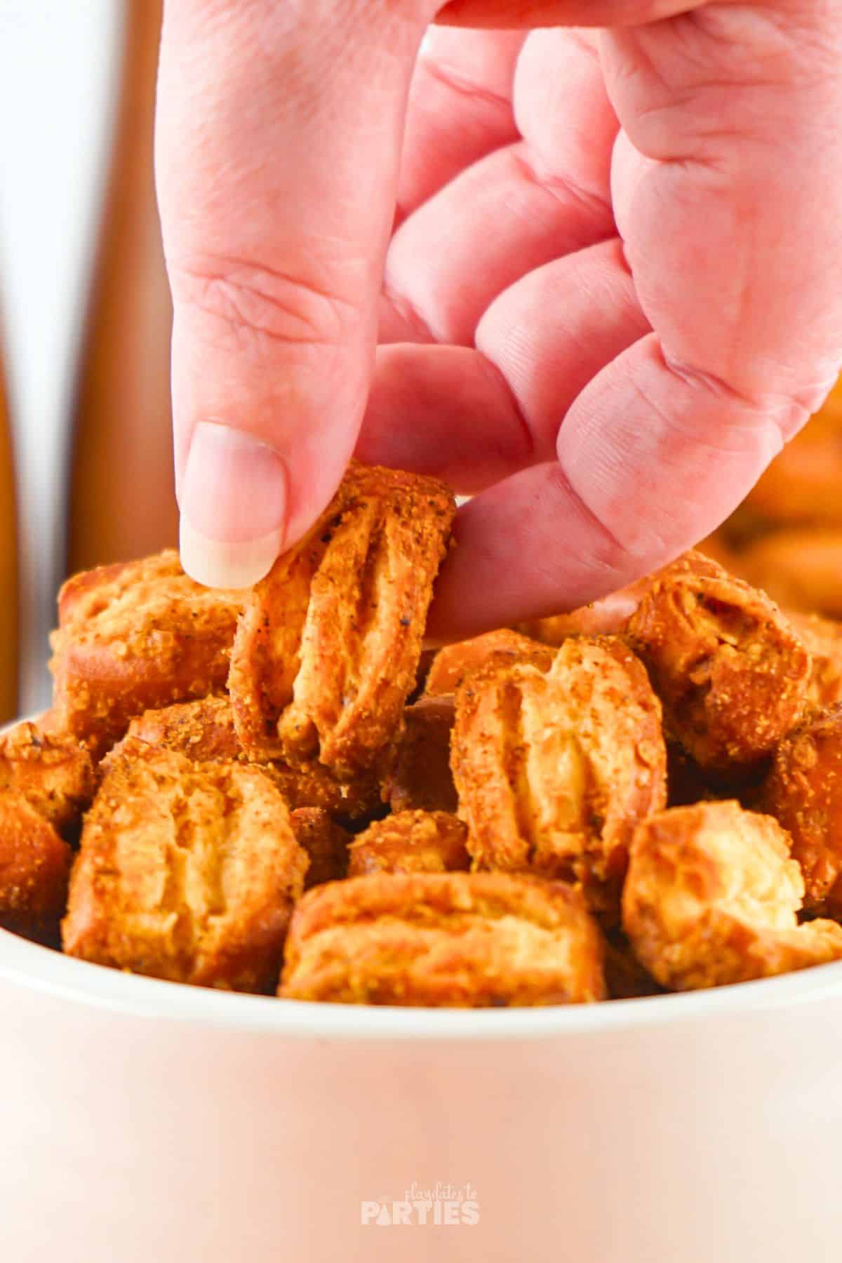 A womans hand grabbing pretzel bites from a bowl.