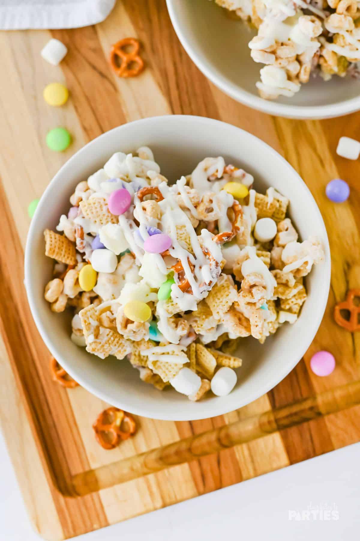 A bowl of Easter snack mix on a wood cutting board.