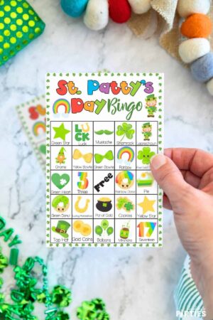 A woman's hand holding a printable St. Patrick's Day bingo card.