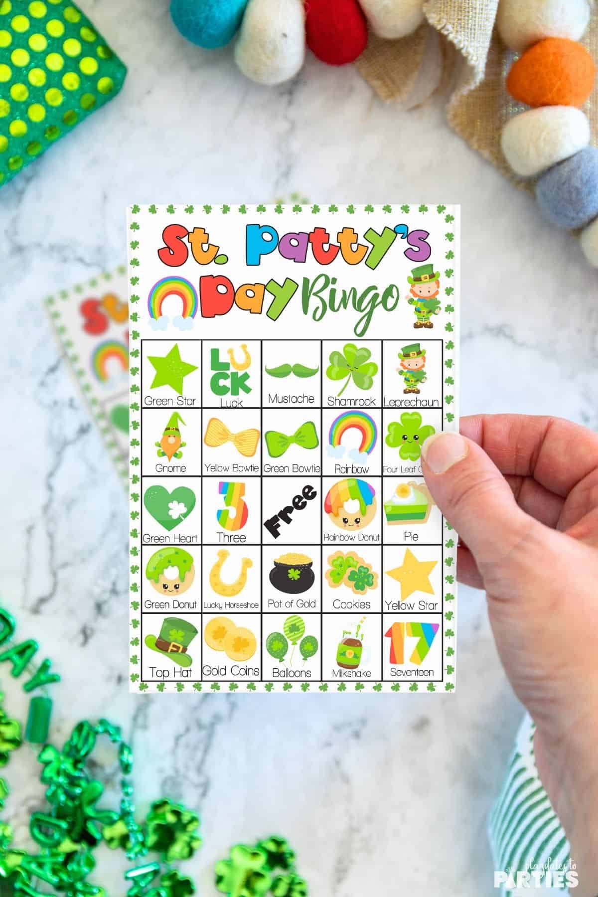 A woman's hand holding a printable St. Patrick's Day bingo card.