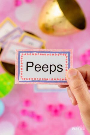 A womans hand holding an Easter charades card that says Peeps.