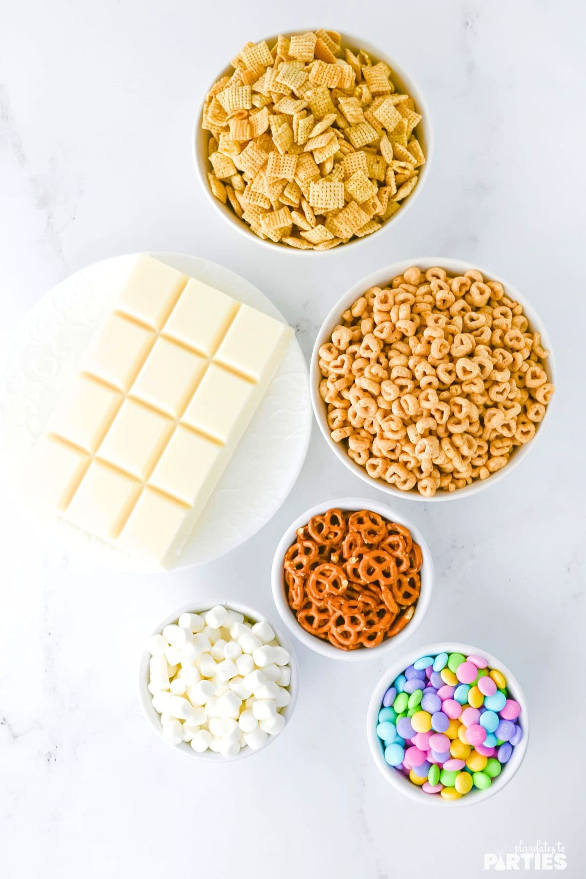 Ingredients include chex mix, cheerios, mini pretzels, candy, marshmallows, and vanilla almond bark.