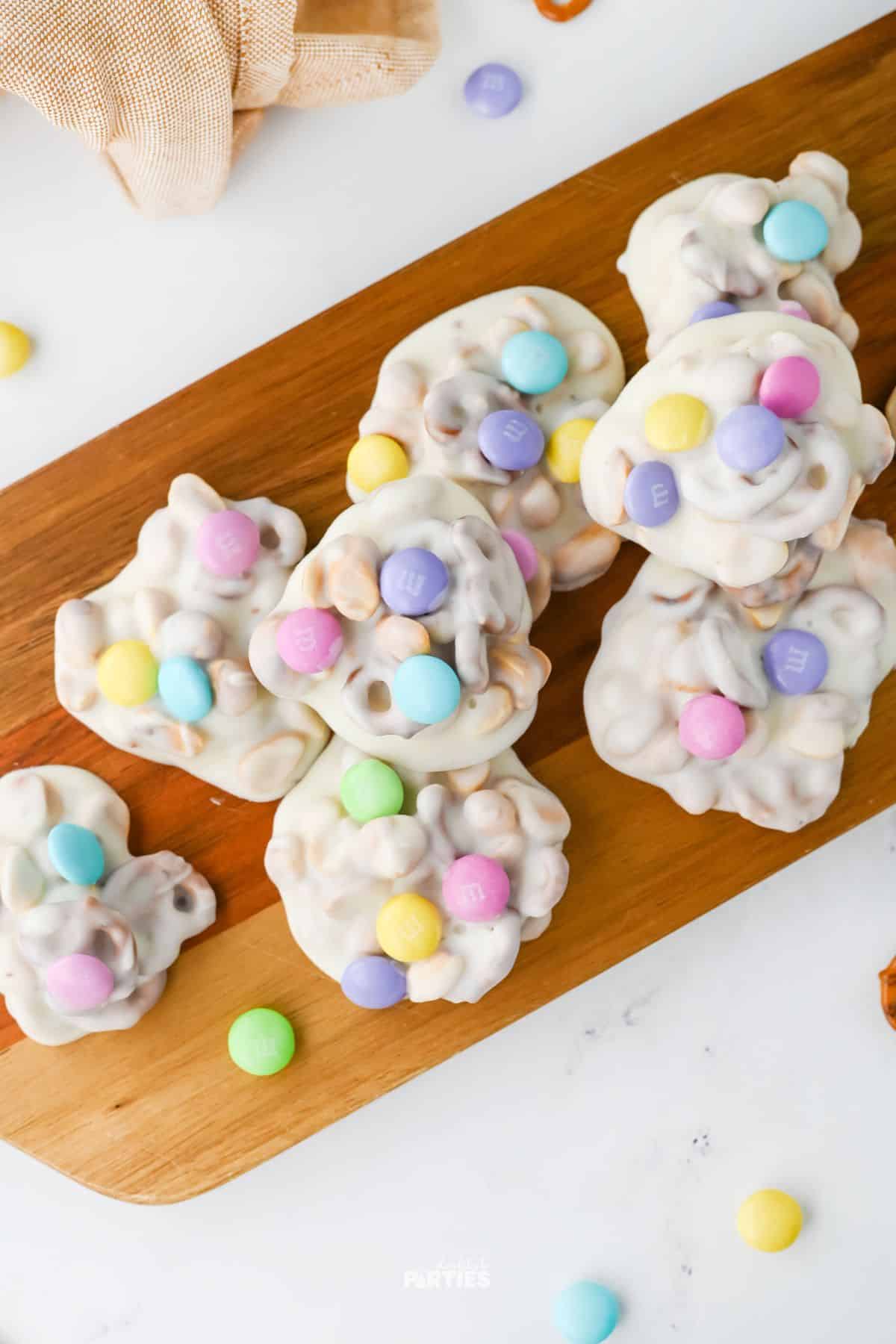 A wood board with candy clusters that are decorated in pastel MandMs.