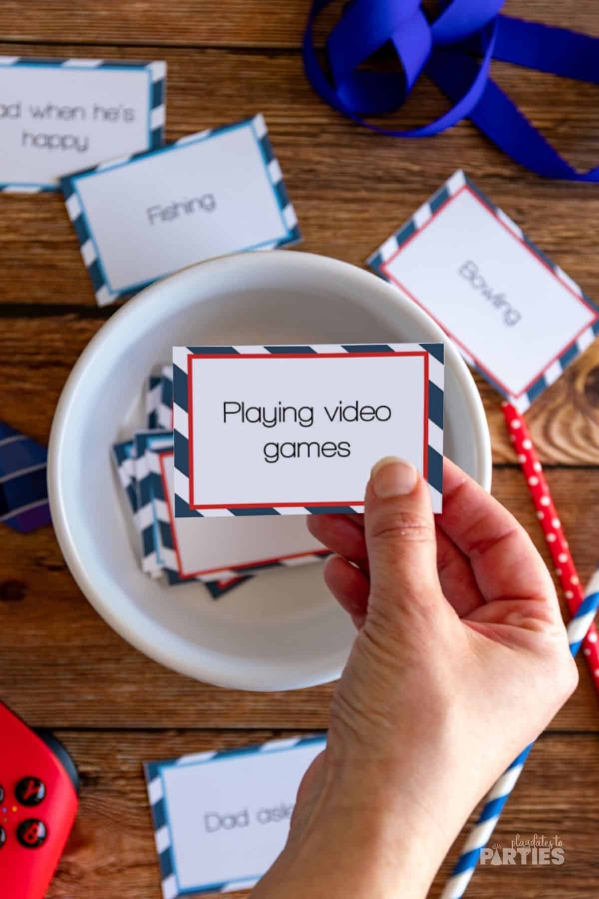A woman's hand holding a charades card that says playing with video games.