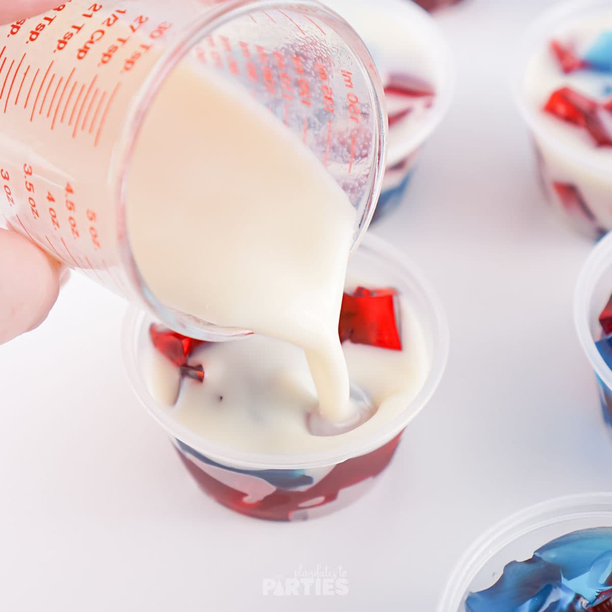 Pouring white gelatin mixture into portioned cups.